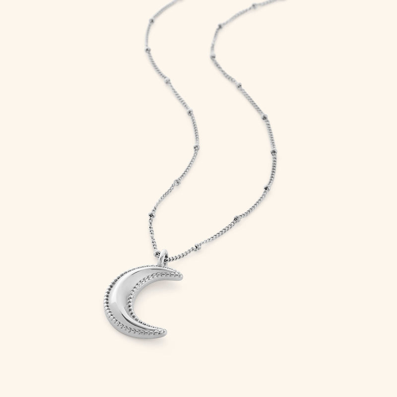 Silver necklace with a dotted crescent moon pendant on a white background