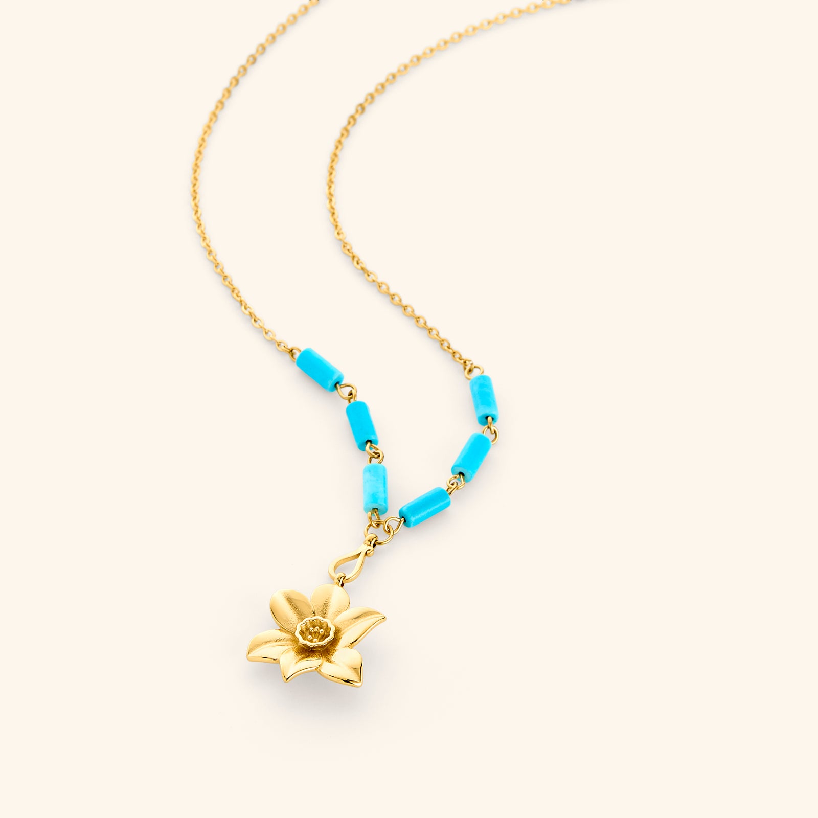 18k gold plated chain necklace on an off-white background. The necklace features a sculpted gold flower pendant resembling a daffodil with a textured center cup. Just above the pendant, the chain is accented with six vibrant blue, tube-shaped turquoise beads—three arranged symmetrically on each side.