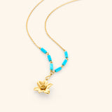 18k gold plated chain necklace on an off-white background. The necklace features a sculpted gold flower pendant resembling a daffodil with a textured center cup. Just above the pendant, the chain is accented with six vibrant blue, tube-shaped turquoise beads—three arranged symmetrically on each side.