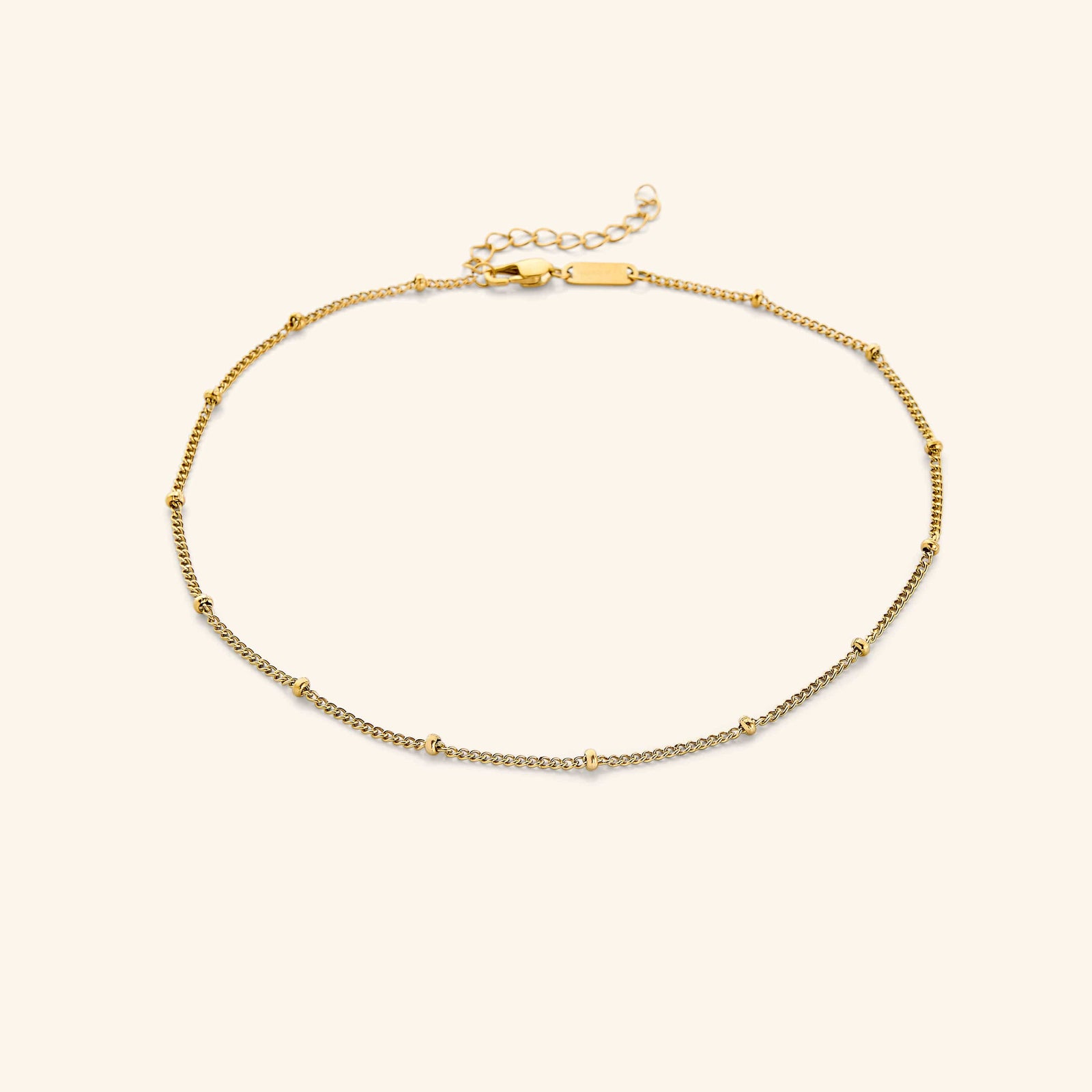 Gold choker with evenly spaced tiny beads, laid flat on a soft beige background.