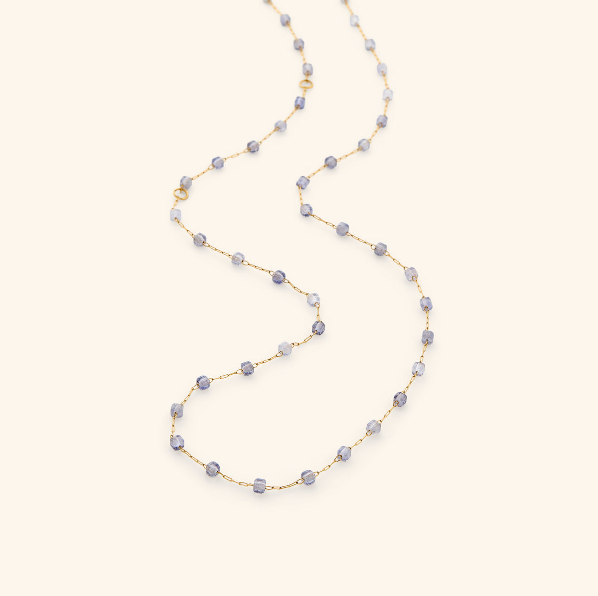 The Essential Iolite Micro Chain by Nominal, featuring a delicate 18k gold-plated chain accented with faceted violet-blue iolite beads, gracefully draped on an off-white background.