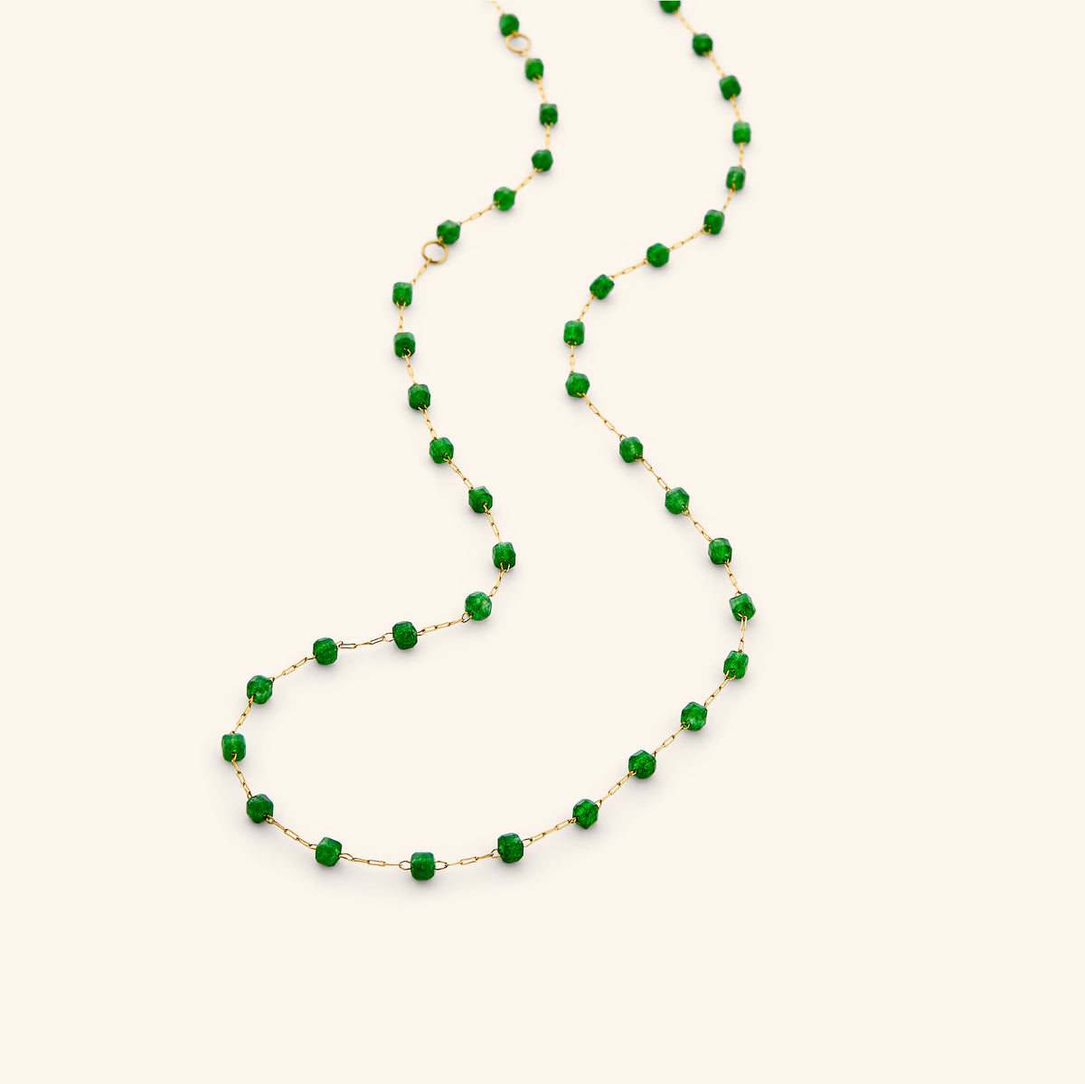 The Essential Emerald Micro Chain by Nominal, featuring a delicate 18k gold-plated chain accented with faceted green emerald beads, draped gracefully on an off-white background.