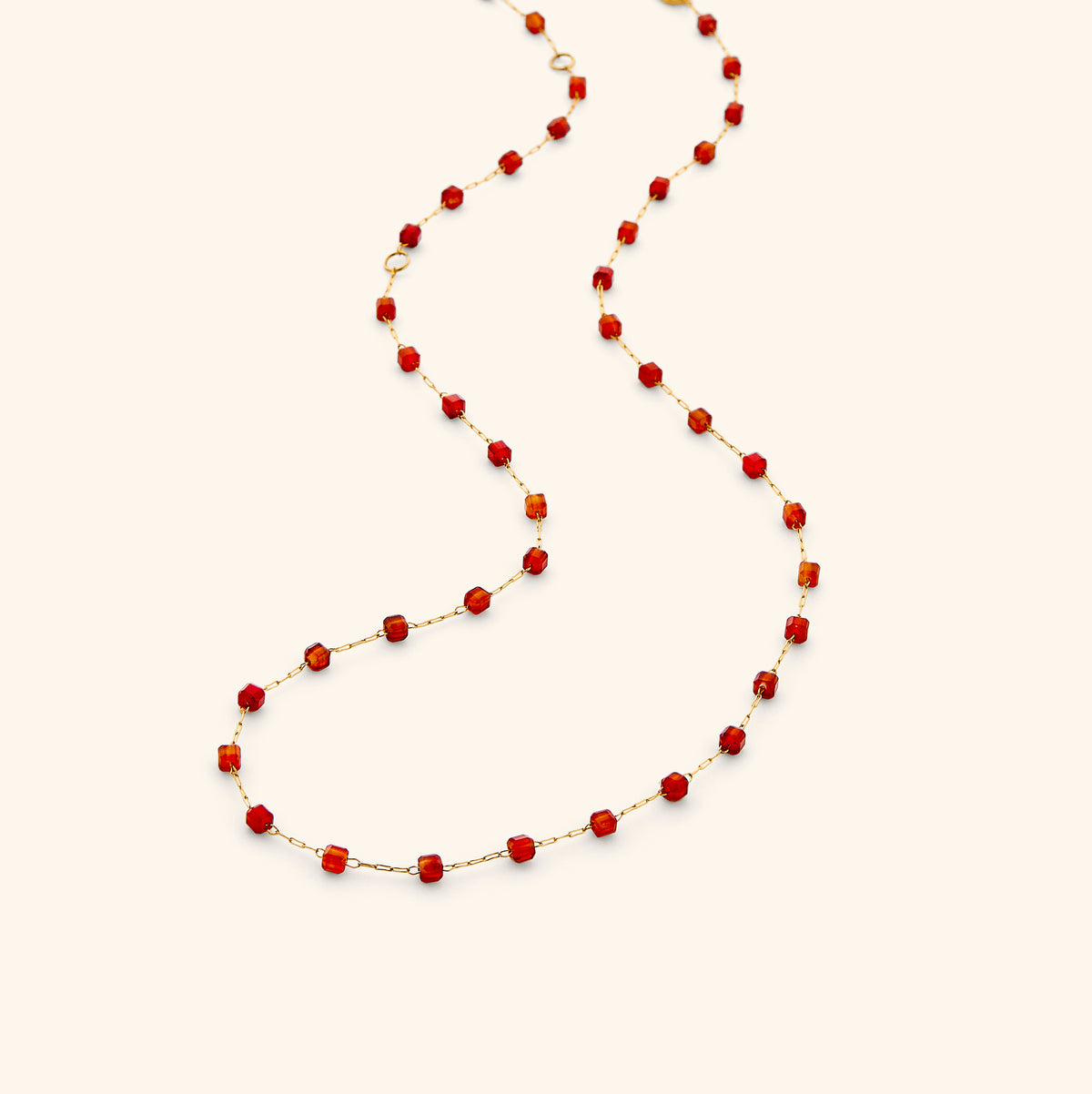 The Essential Red Agate Micro Chain by Nominal, featuring a delicate 18k gold-plated chain accented with faceted rich red agate beads, gracefully draped on an off-white background.