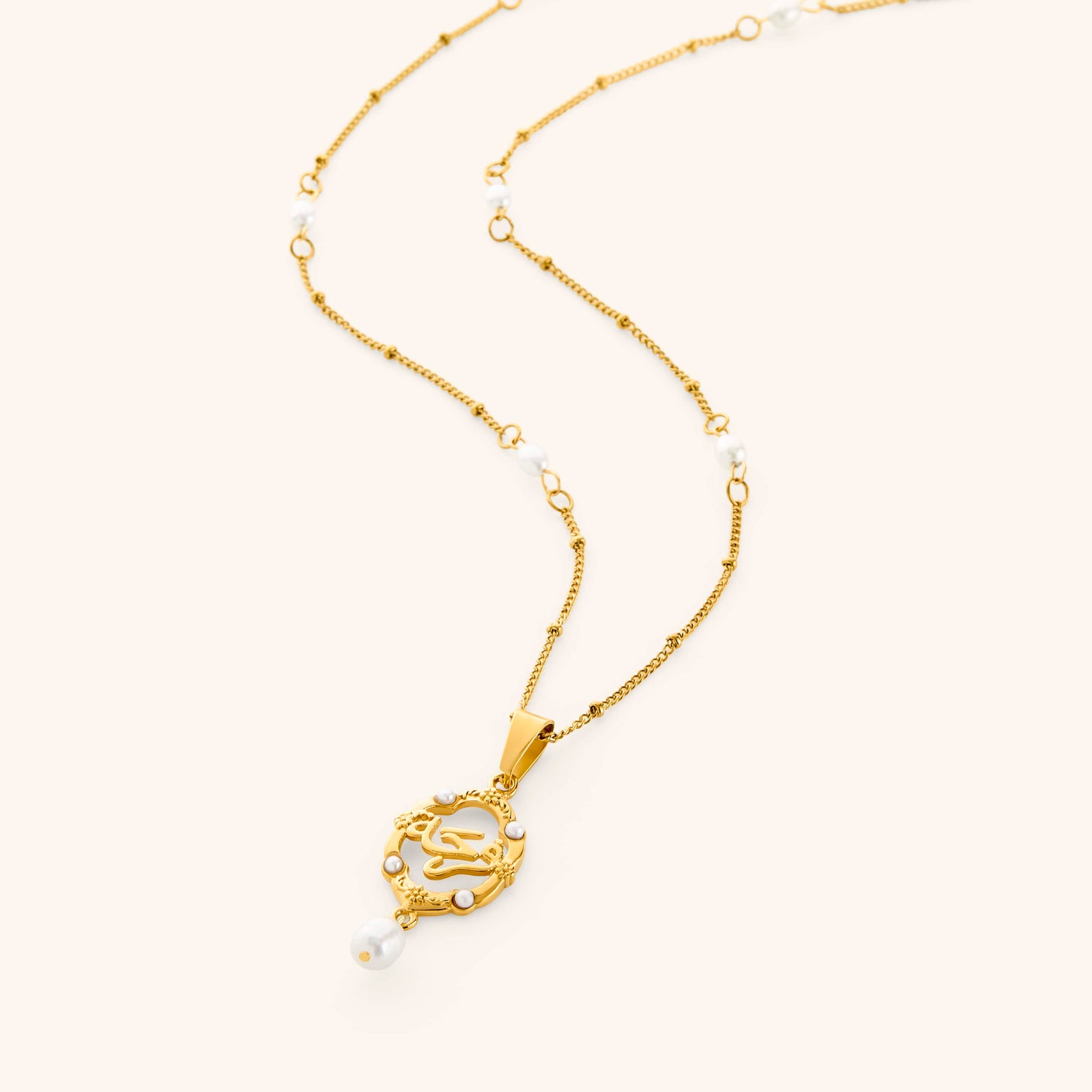 Flat lay of an 18k gold plated necklace that features pendant that spells out "فرح" (joy in Arabic), framed in an ornate gold border with floral detailing and freshwater pearls nestled throughout the entire piece. A single pearl drop finishes the pendant at the bottom, while more pearls line the chain itself.