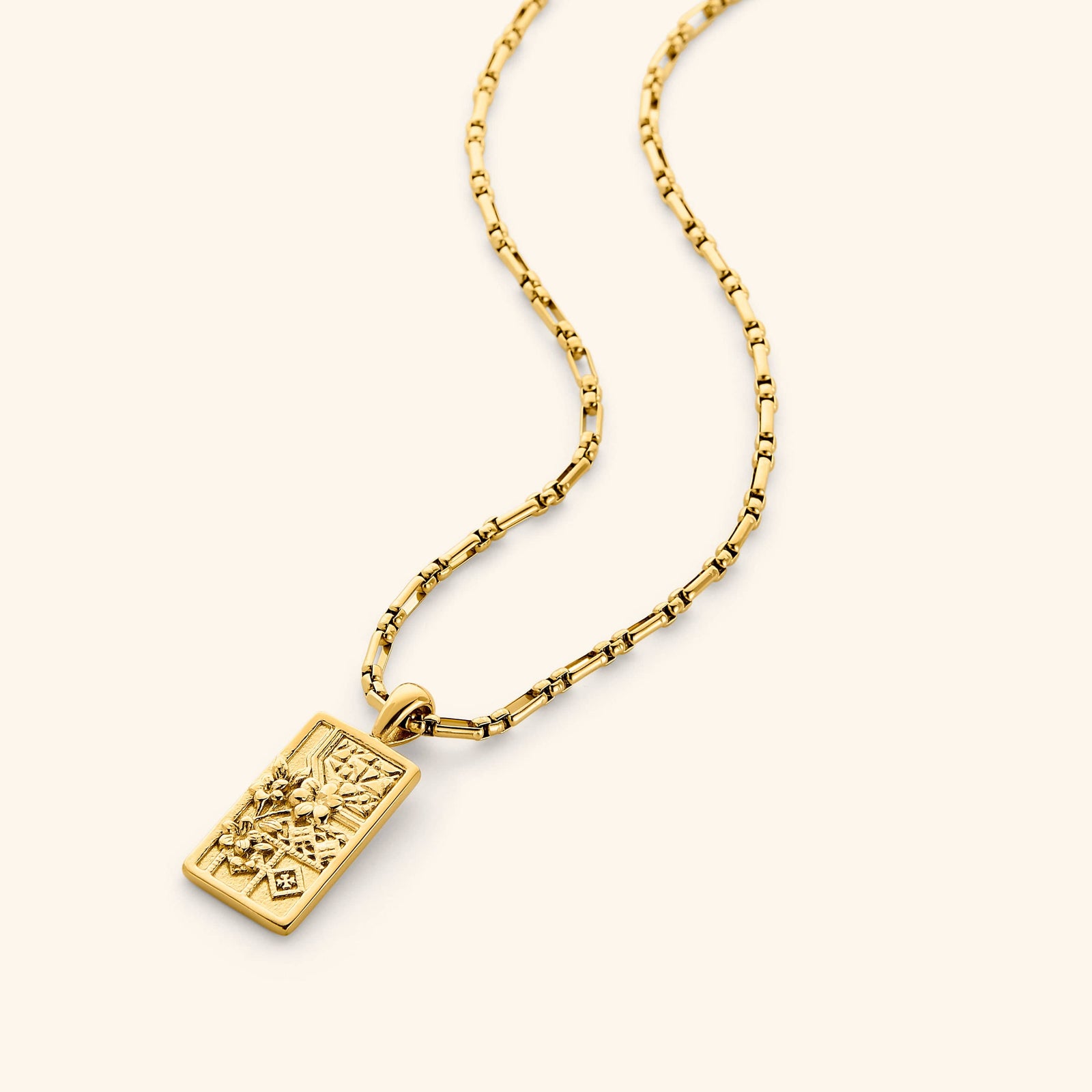 In the photo, a rectangular 18K gold plated pendant that features design Inspired by the mosaic patterns of Damascus found in the mosques and courtyards, blooming with the national flower of Syria: the jasmine on a gold chain.