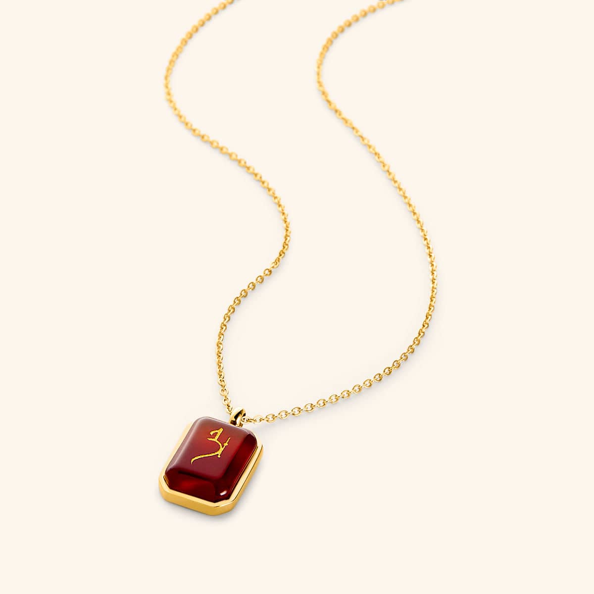 Gold chain necklace with a rectangular red agate stone pendant engraved in Arabic calligraphy reading "Love," framed in a polished gold border, displayed on a light background.