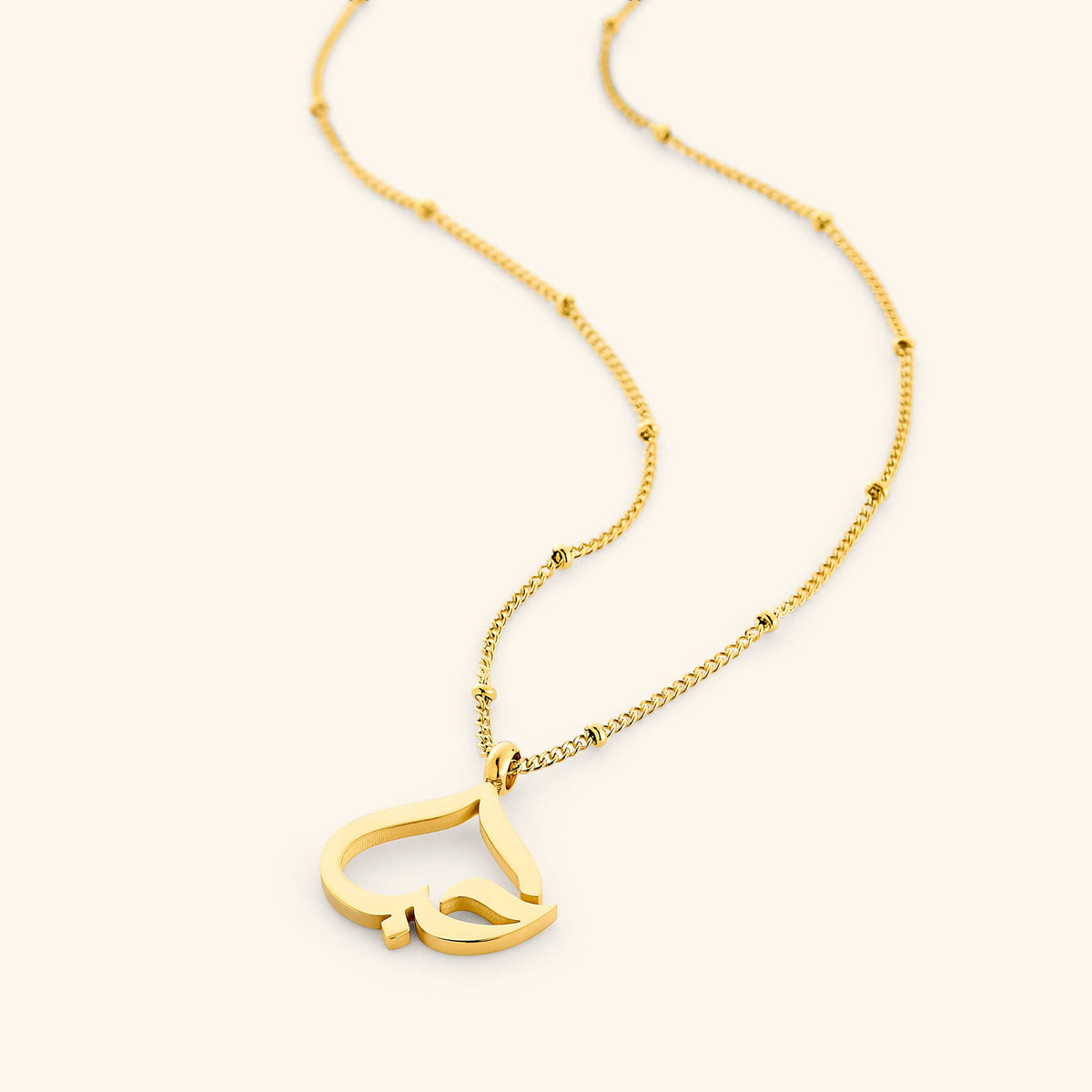 Flat lay of an 18k gold plated necklace. The  'Love' Calligraphy Necklace features a hanging heart-shaped pendant with the Arabic word for 'love' (حب) 