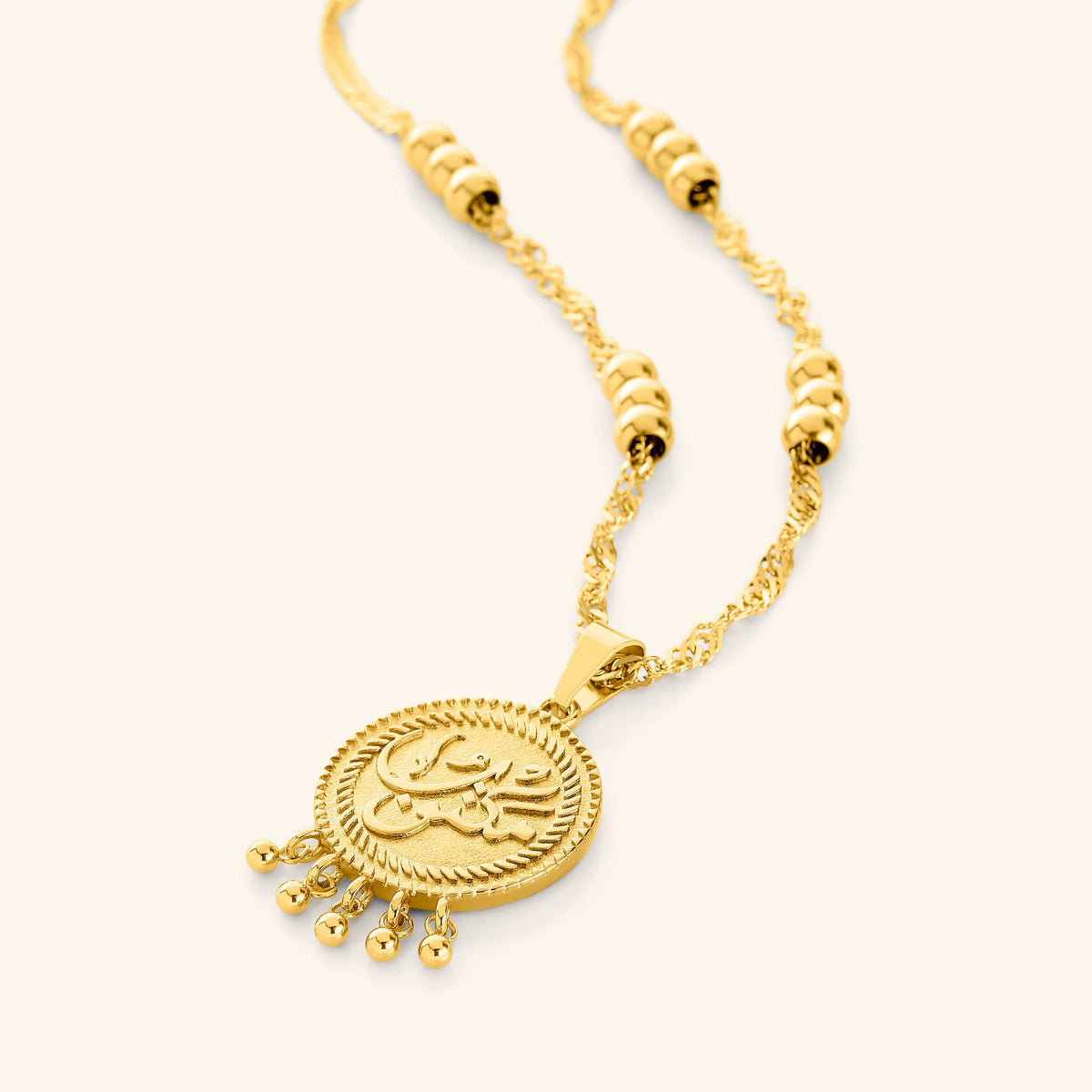 An 18k gold plated necklace that features a coin pendant with the inscription: مكتوب—"Maktub", twisted chains, burst orbs, and the delicate dangling dots add movement and elegance, 