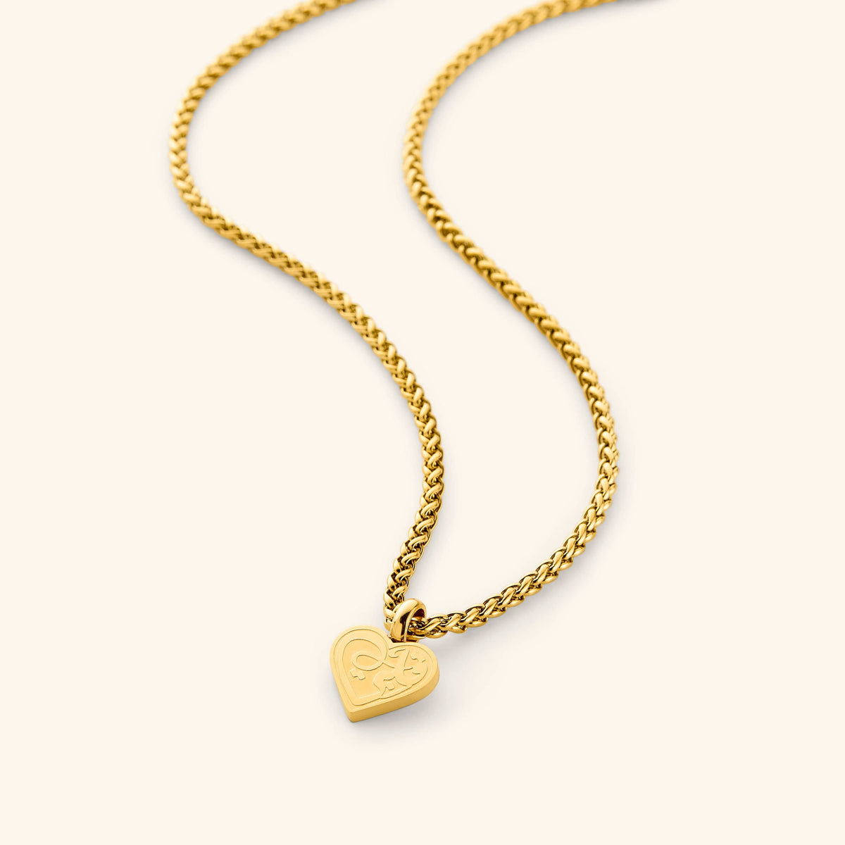 A close-up of the "Piece of Me" Daughter Necklace in 18K gold plating, featuring a minimal heart-shaped charm engraved with the Arabic word "qalbi" ("my heart") in elegant calligraphy. The pendant hangs from a delicate wheat chain.
