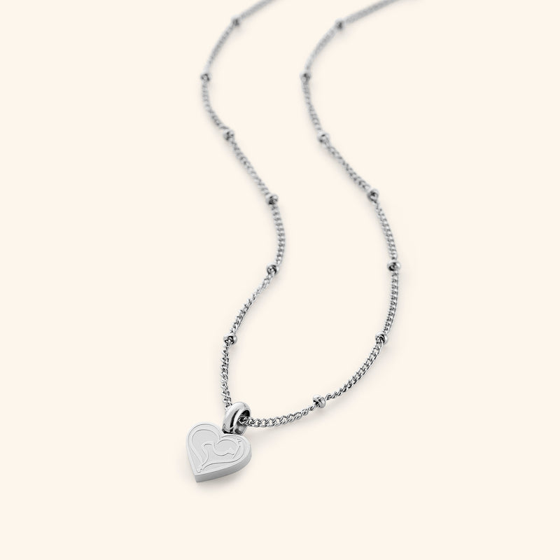 The Mother Love Necklace in a polished silver finish pimage_ displaying a heart-shaped charm with the Arabic inscription "Ummi pimage_" suspended from a sleek dotted chain pimage_ emphasizing its refined craftsmanship.