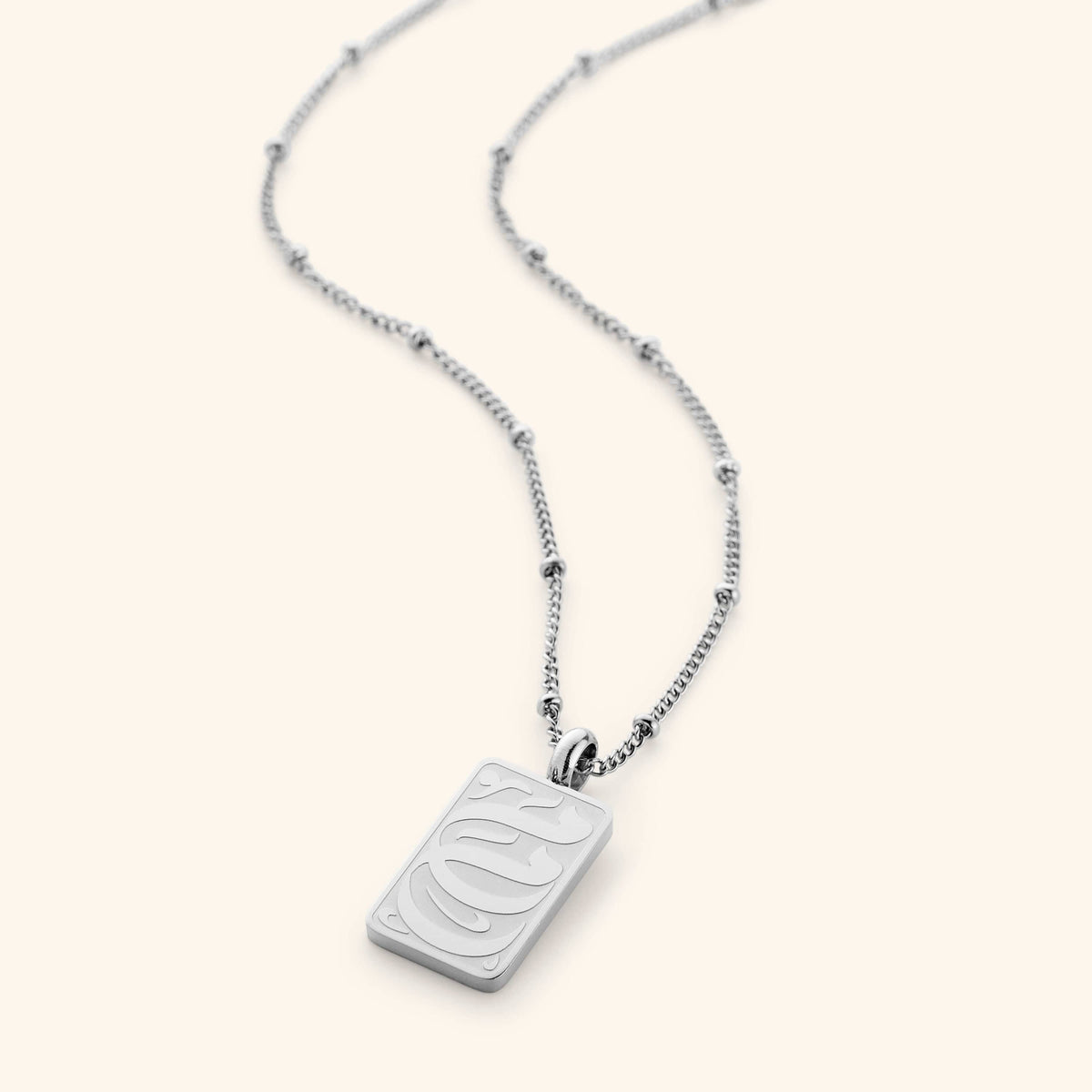 The "My Mother Tag Necklace" in a polished silver finish, displaying a rectangular pendant with the Arabic inscription "Ummi," suspended from a sleek dotted chain, emphasizing its refined craftsmanship.