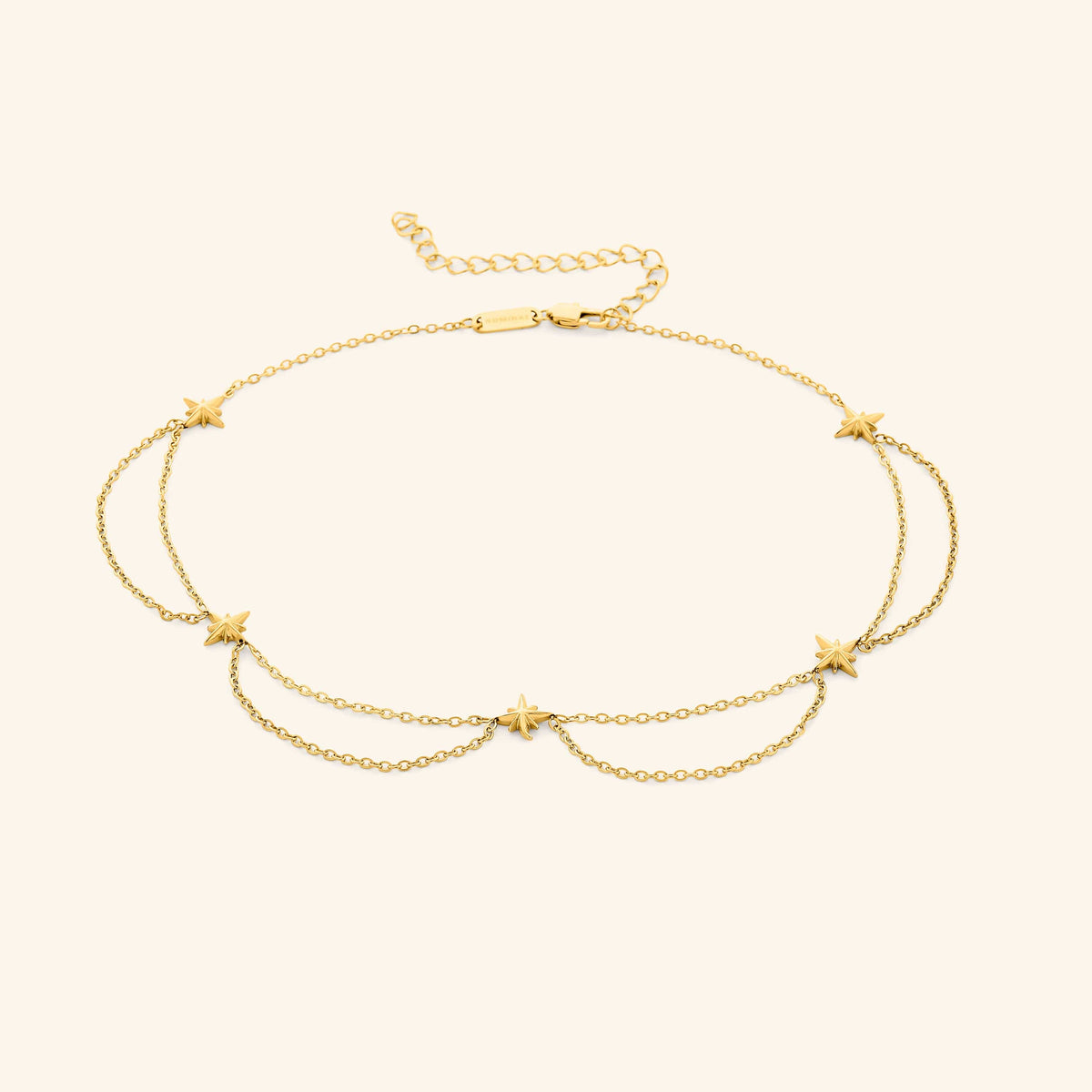 Flat lay of the 18k gold plated necklace that features north stars all along the chain, drooping chains connecting each one.