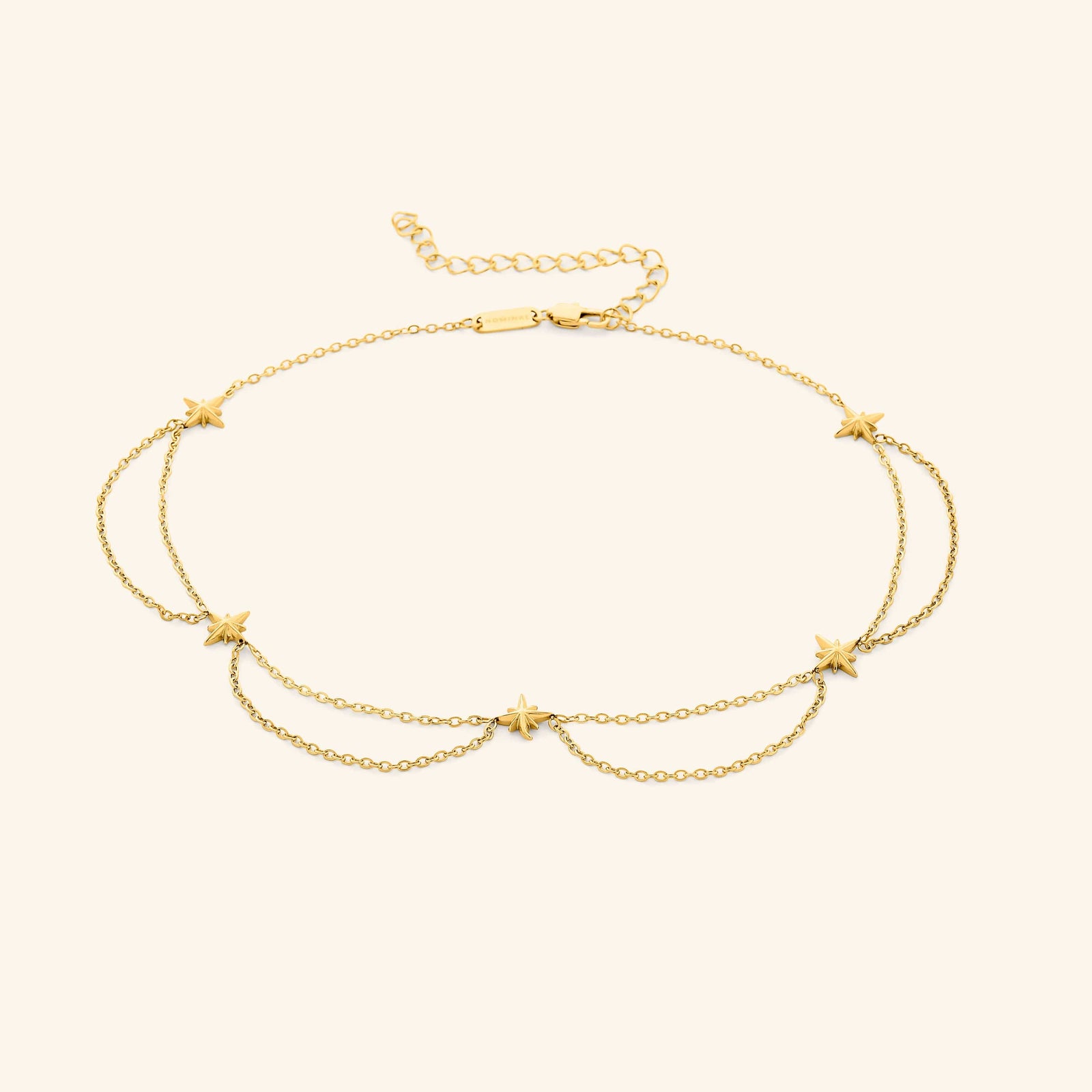 Flat lay of the 18k gold plated necklace that features north stars all along the chain, drooping chains connecting each one.