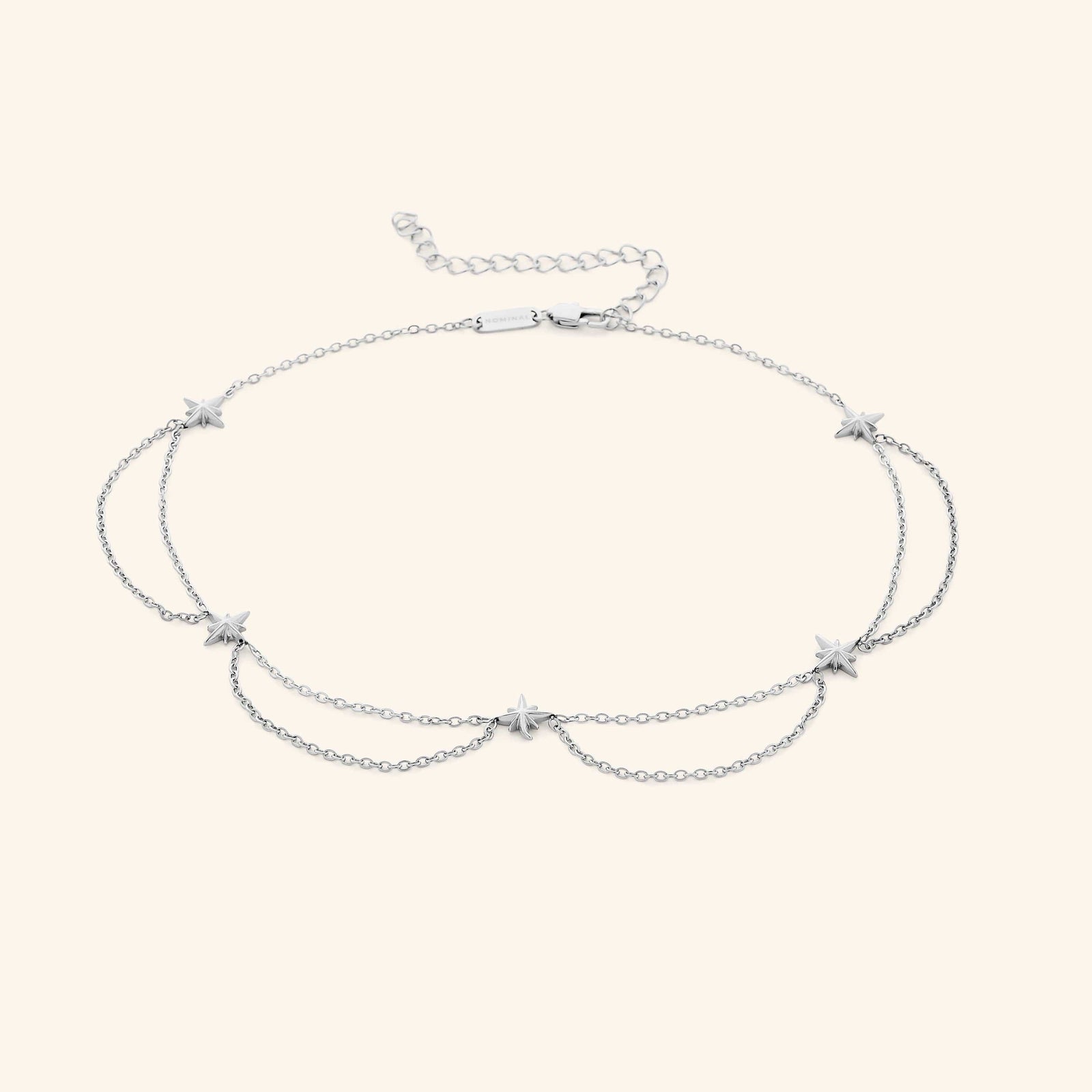 Flat lay of the silver necklace that features north stars all along the chain, drooping chains connecting each one.