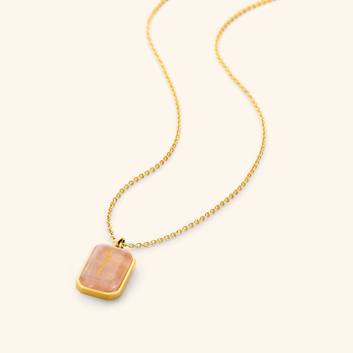 Gold chain necklace with a rectangular rose quartz stone pendant engraved in Arabic calligraphy reading "Sabr" (patience), framed in a polished gold border, displayed on a light background.