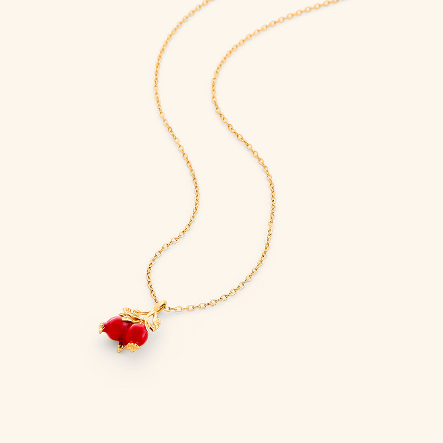 The Pomegranate Necklace by Nominal, featuring an 18k gold-plated delicate chain paired with a vibrant red pomegranate fruit and gold leaf pendant, displayed on an off-white background.