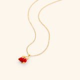 The Pomegranate Necklace by Nominal, featuring an 18k gold-plated delicate chain paired with a vibrant red pomegranate fruit and gold leaf pendant, displayed on an off-white background.