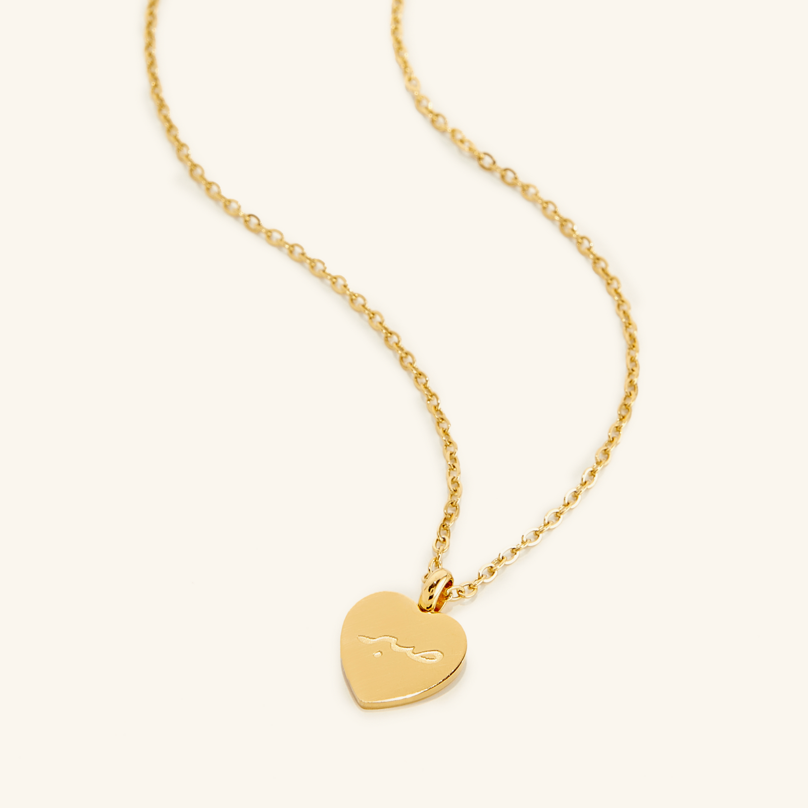 Photo of an 18k gold plated necklace with a heart shaped pendant that features an engraving of the the word "Patience" in Arabic Calligraphy