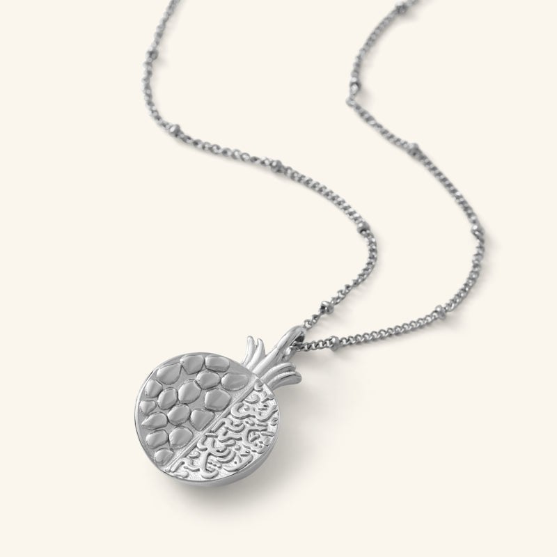 Seeds of Gratitude Necklace in silver featuring a pomegranate-shaped pendant with engraved seeds on one half and Arabic calligraphy on the other.