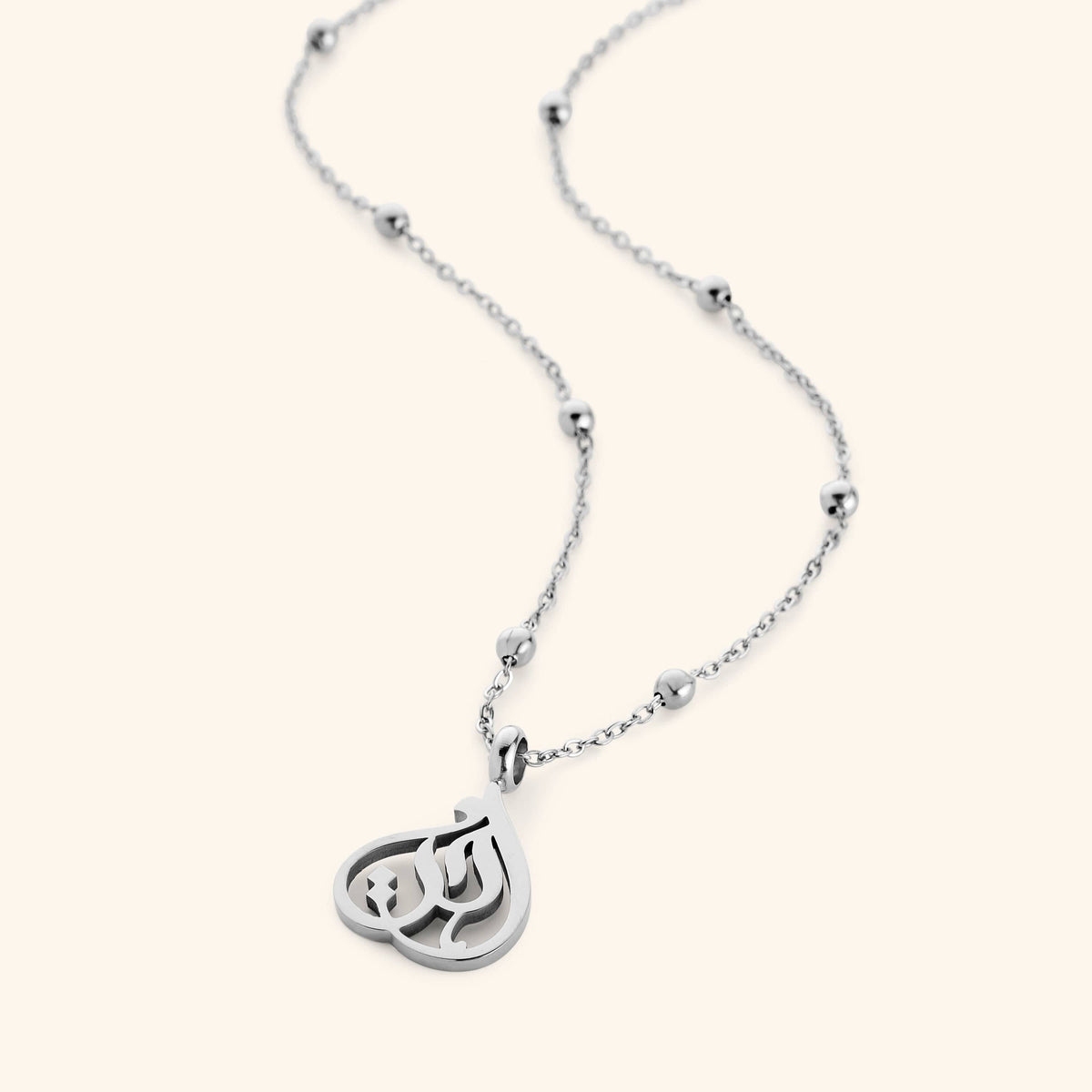 Silver necklace with beaded chain and teardrop-shaped pendant featuring Arabic calligraphy spelling “Sister”, photographed flat against a cream background.