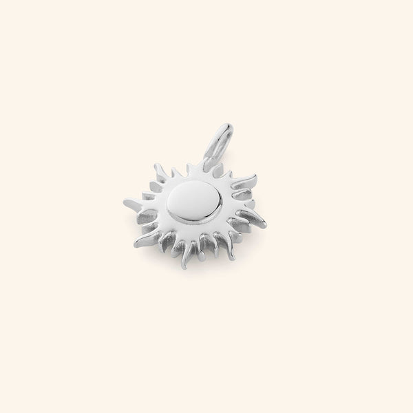 Silver sunshine charm, displayed flat on a cream-colored background.