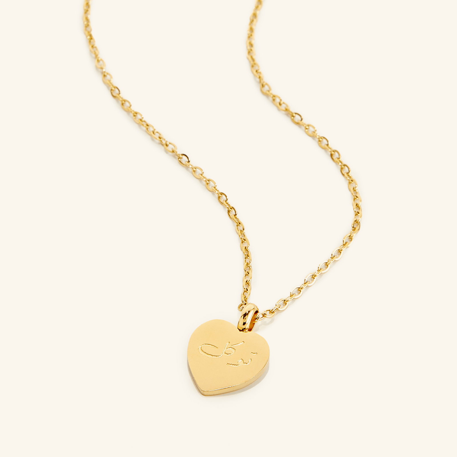 Photo of an 18k gold plated necklace with a heart shaped pendant that features an engraving of the the word Trust in Arabic Calligraphy