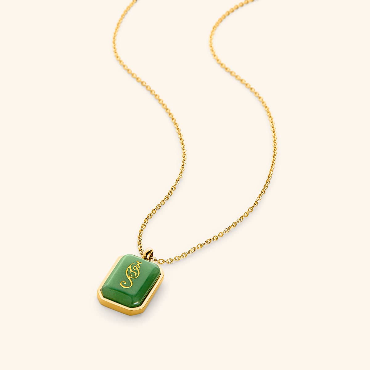 Gold chain necklace with a rectangular green aventurine stone pendant engraved in Arabic calligraphy reading "Tawakkul" (trust), framed in a gold border, displayed on a light background.