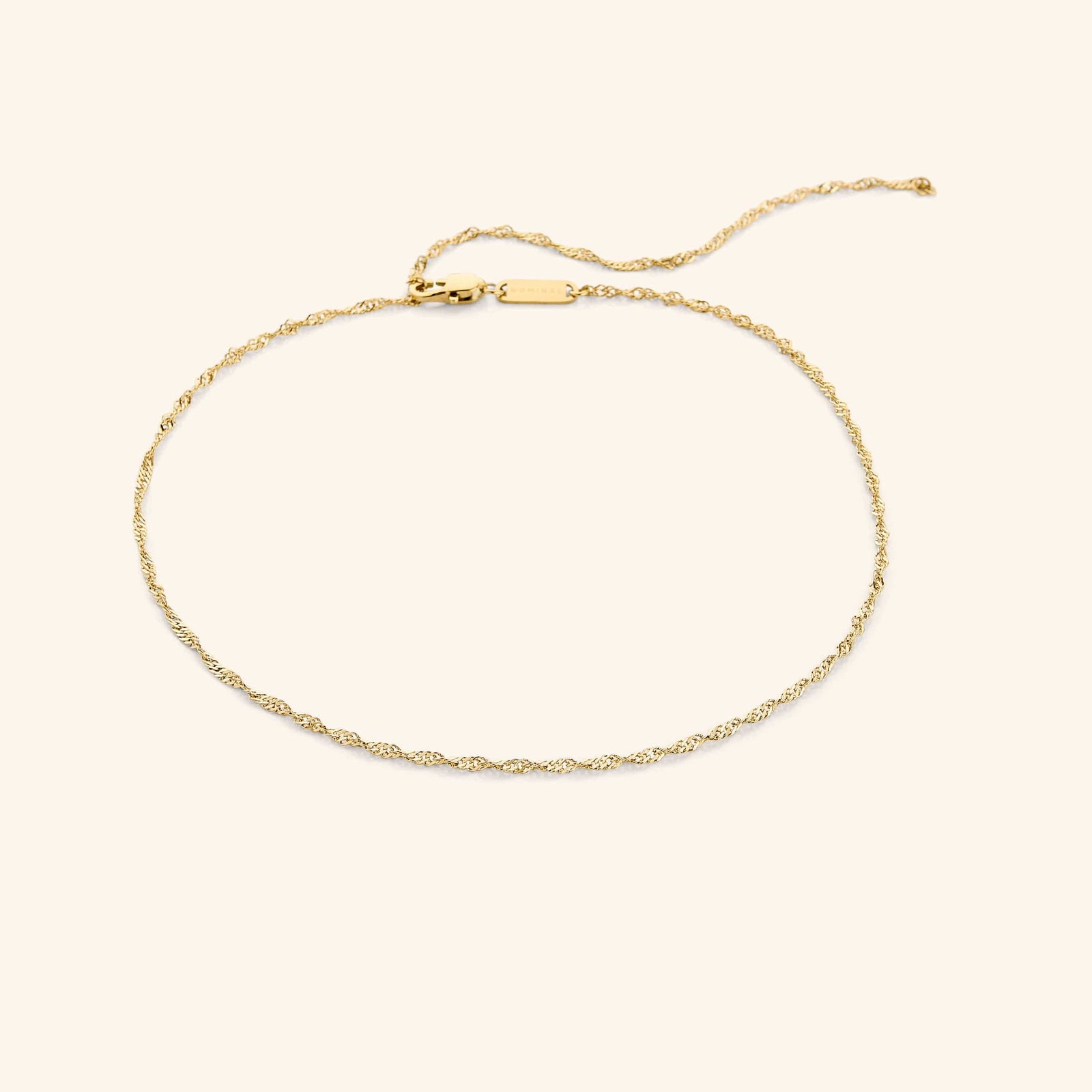 Gold twisted chain choker laid flat on a neutral beige background.