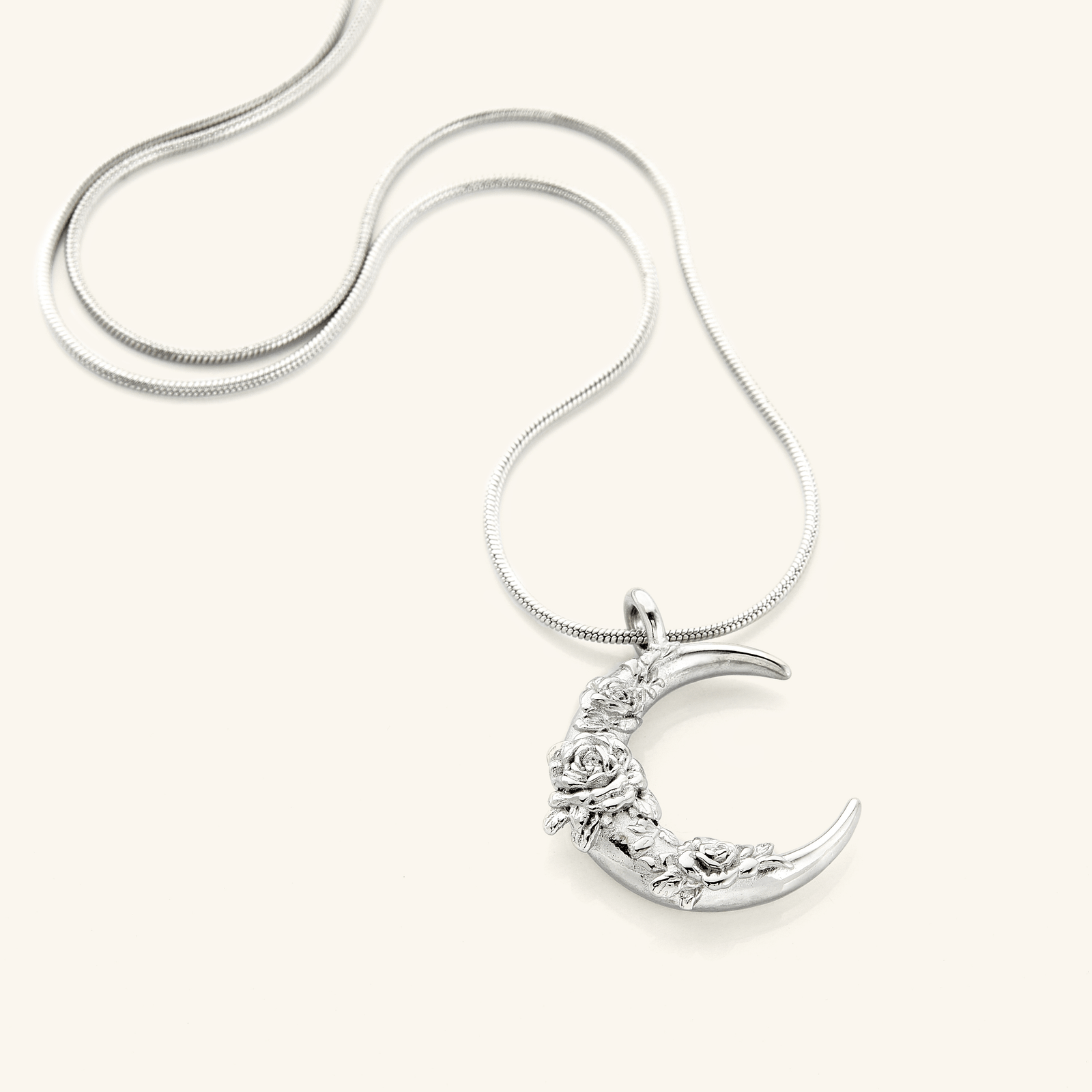 The Damask Rose Crescent Necklace in a polished silver finish, showcasing a crescent moon pendant with detailed damask rose engravings, hanging from a slender silver chain.