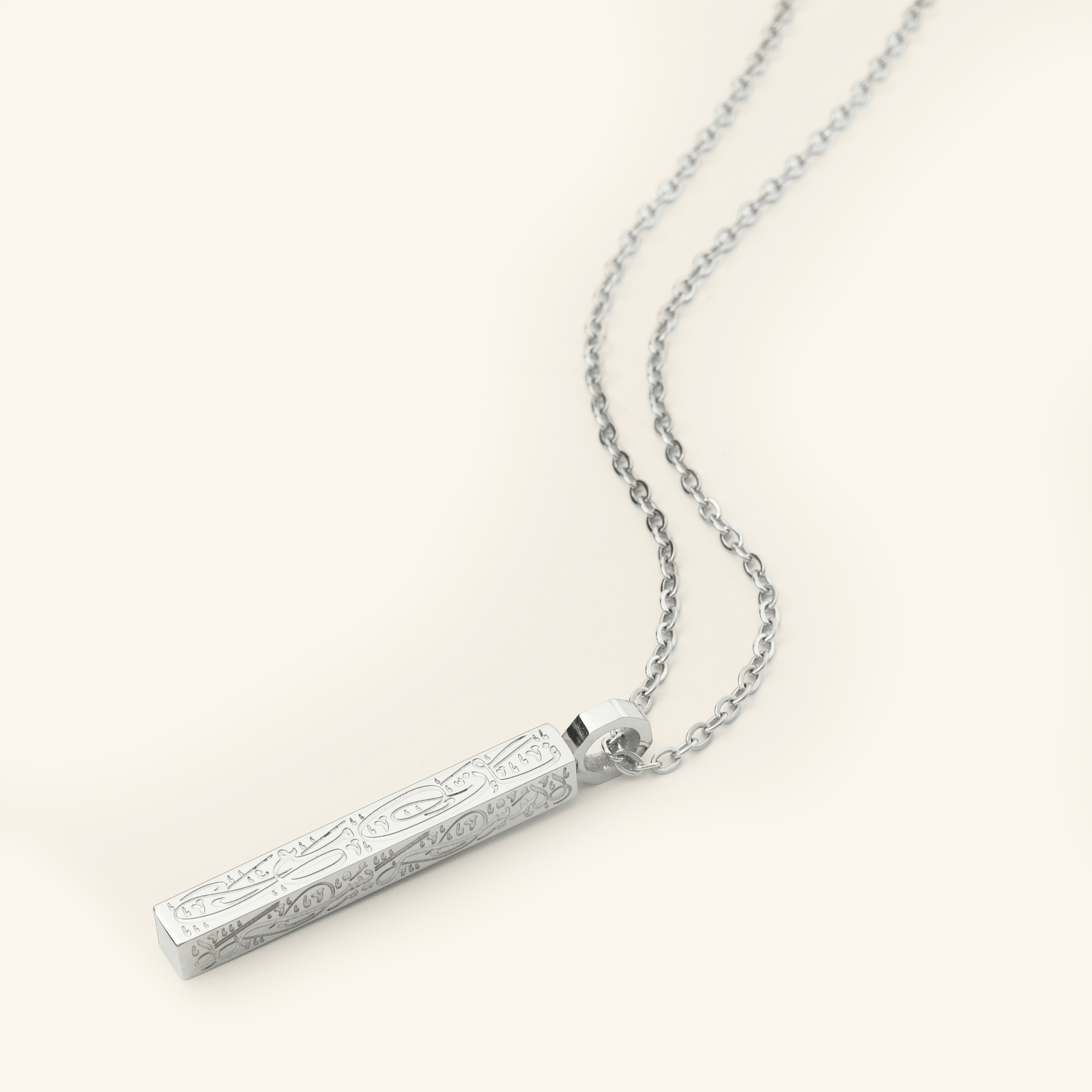 Photo of a silver necklace that features the Arabic Calligraphy of  'with every hardship comes ease' that is engraved intricately all along this timeless bar pendant. 