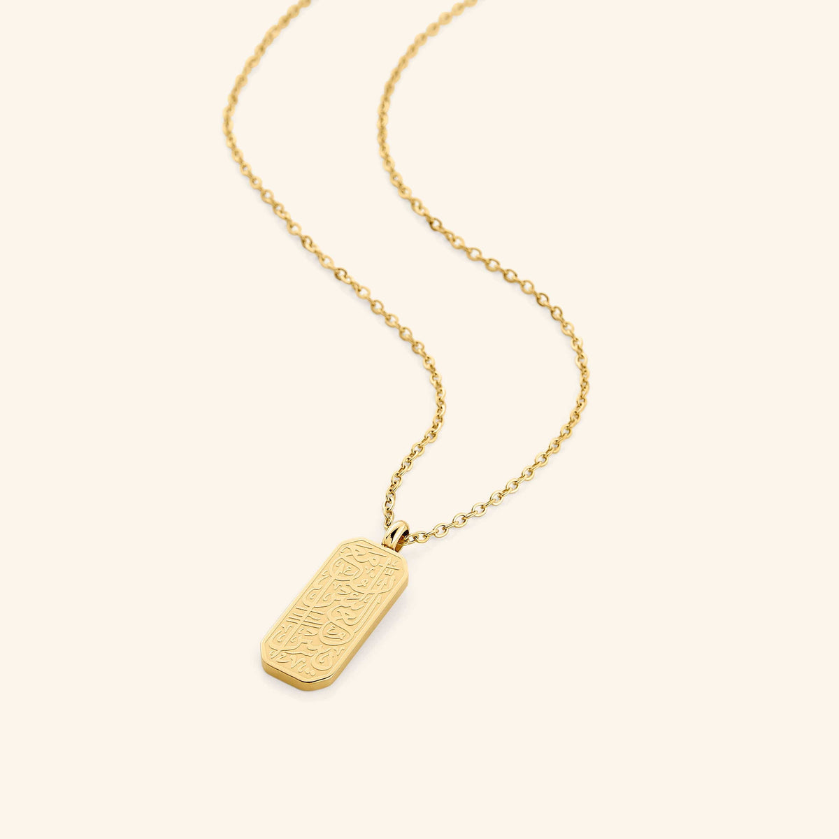 Flat lay of an 18k gold plated necklace that features "Verily with Every Hardship Comes Ease"  calligraphy design on a unique tag-shaped pendant. 