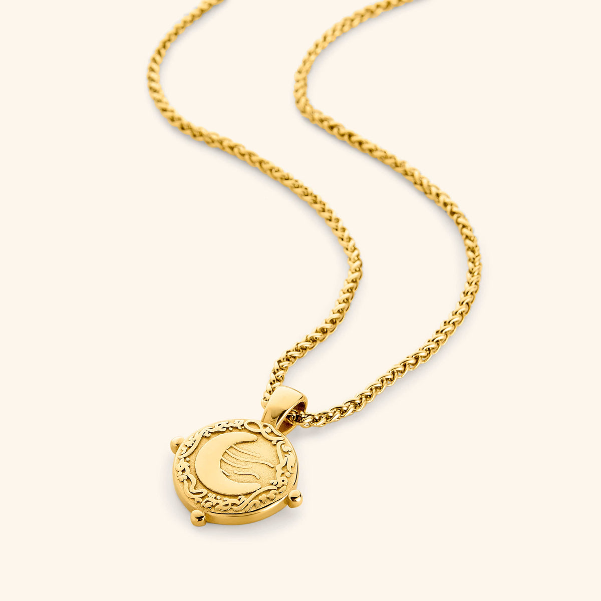 Gold necklace with a round pendant featuring the engraved phrase 'What you seek is seeking you' in Arabic calligraphy. The design includes a raised crescent moon and a flowing motif, framed with vine detailing and three small bead accents around the border. 