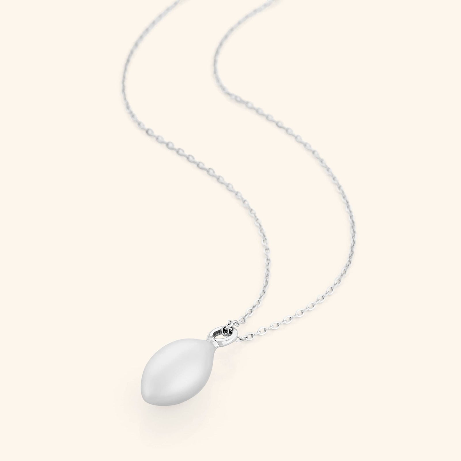 Flat lay of a silver necklace with a pendant that is made in the actual spherical shape of an olive and inspired by the beautiful olive trees of Palestine