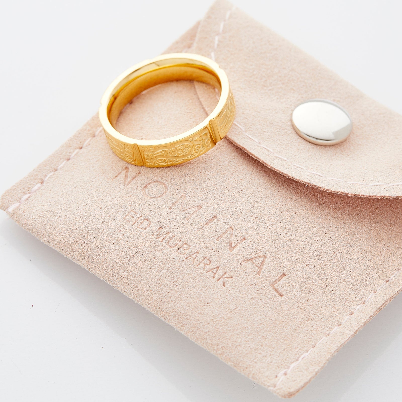 Gold Five Pillars Ring resting on a beige suede pouch debossed with the word "NOMINAL" and "EID MUBARAK" in small lettering.