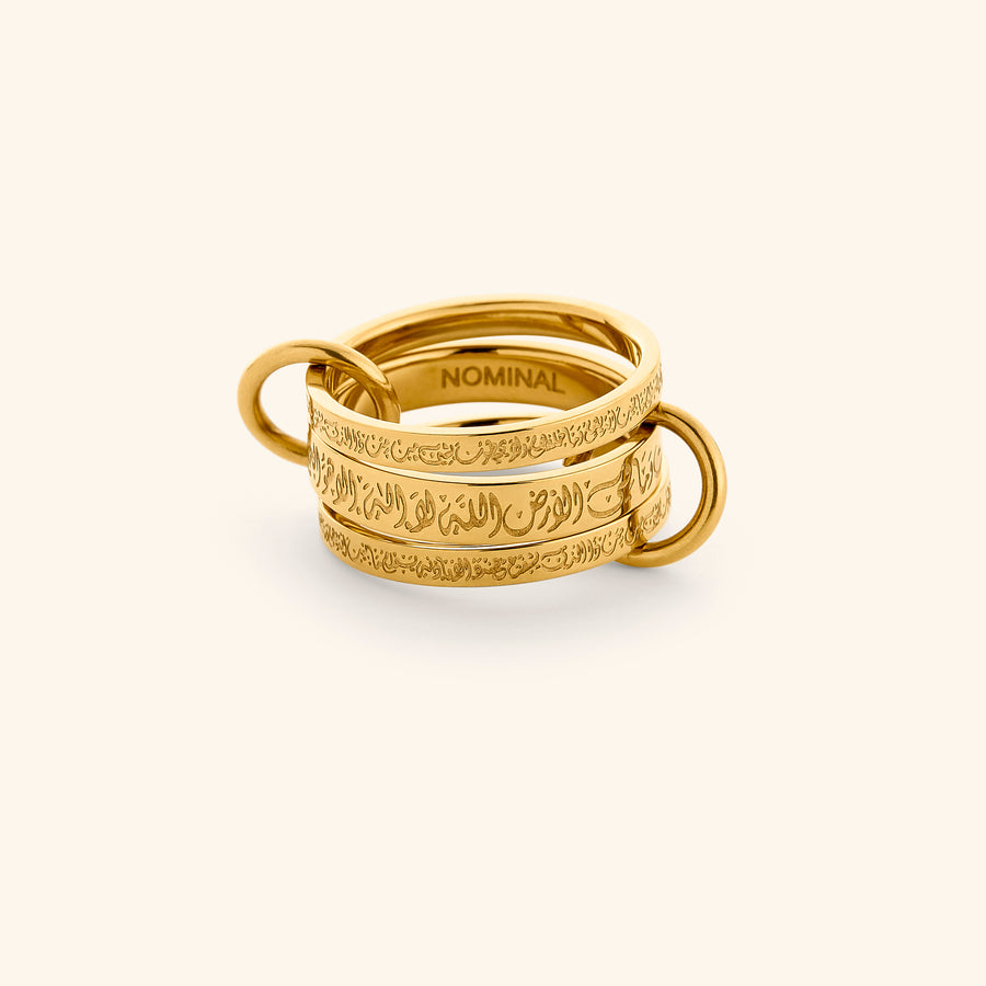 The Ayatul Kursi Ring Stack by Nominal, featuring interlocking 18k gold-plated bands intricately engraved with Arabic calligraphy and connected by delicate side loops, displayed on an off-white background.