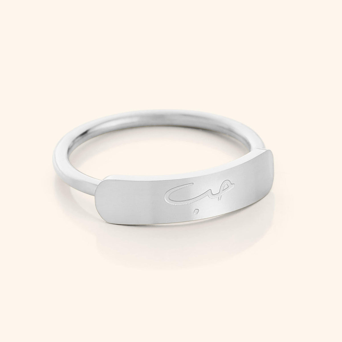 Close-up of a slim silver ring with a rectangular bar centerpiece engraved with the Arabic word meaning "love," shown on a plain background.