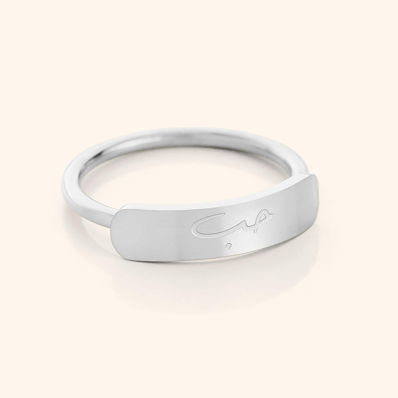 Close-up of a slim silver ring with a rectangular bar centerpiece engraved with the Arabic word meaning "love," shown on a plain background.