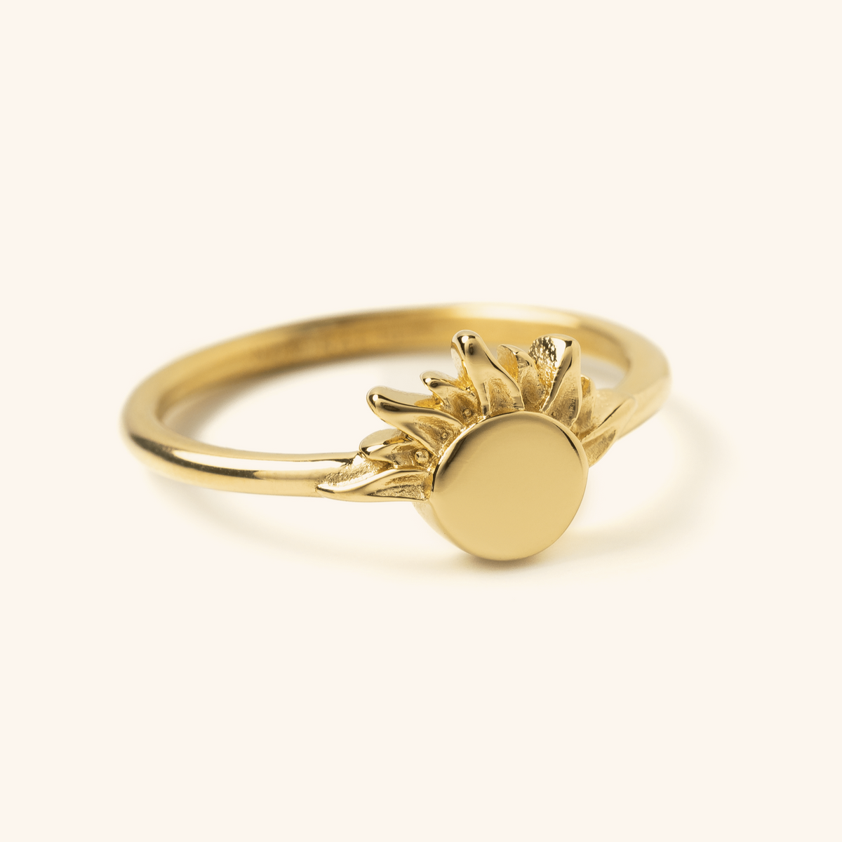 Gold ring featuring a circular sun design with textured rays extending outward, photographed against a neutral background.
