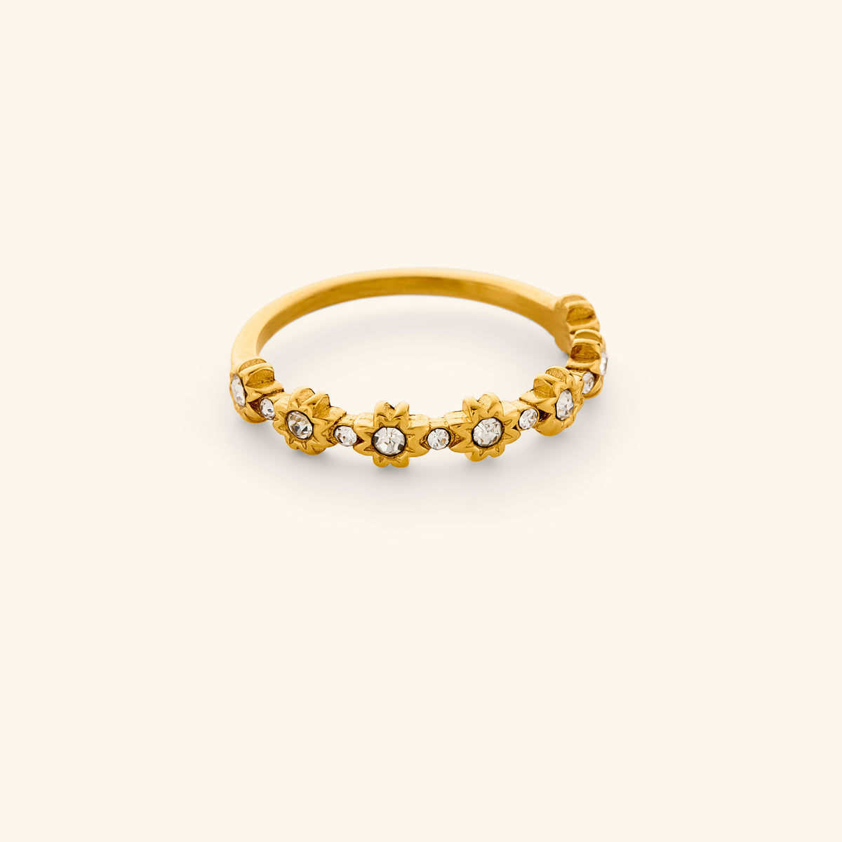 The Bezel Garden Ring by Nominal, crafted with an 18k gold-plated finish featuring delicate bezel-set crystal flower motifs along the band, displayed on an off-white background.