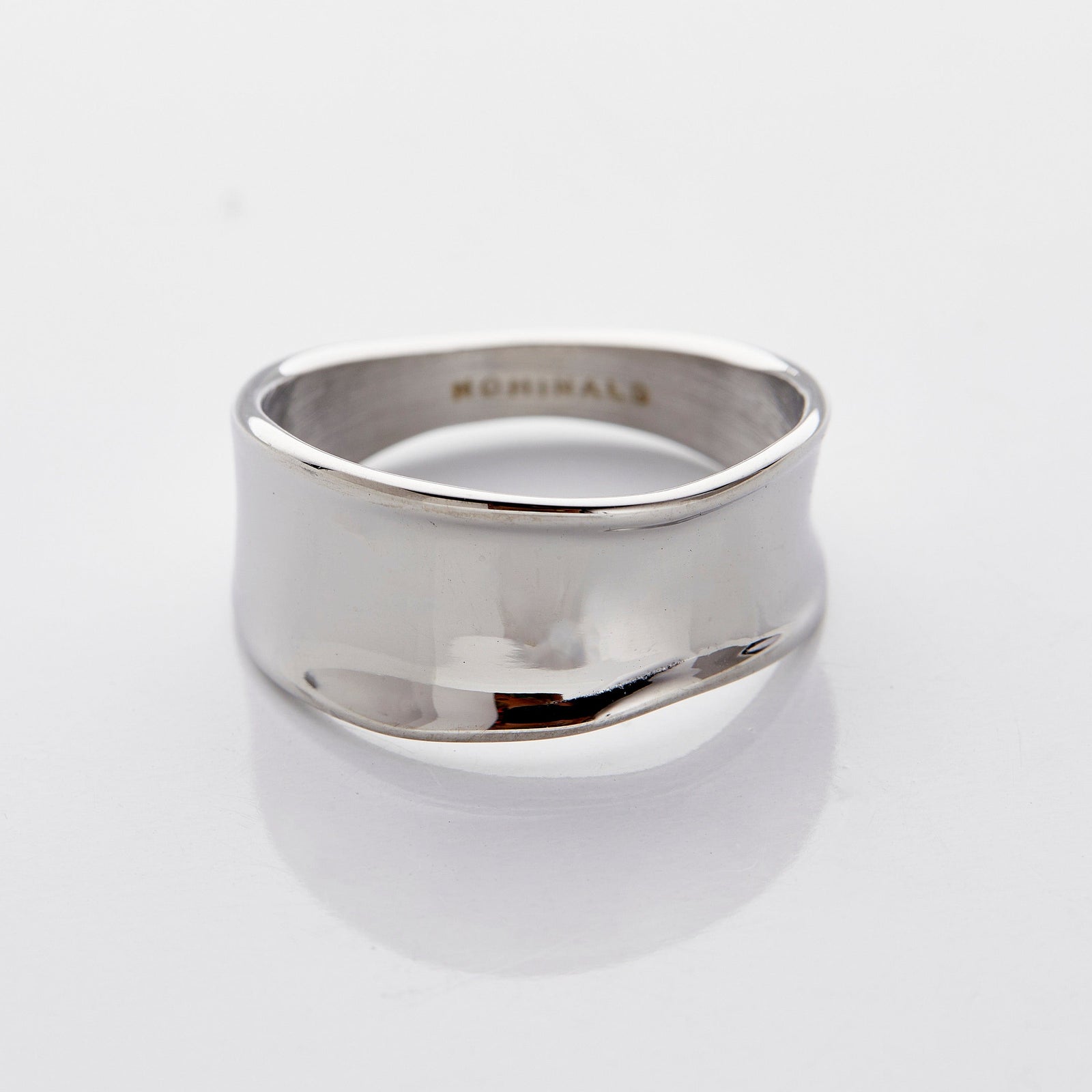 Close-up of a wide, wavy silver band ring with a smooth, melted-like design, photographed against a neutral background.