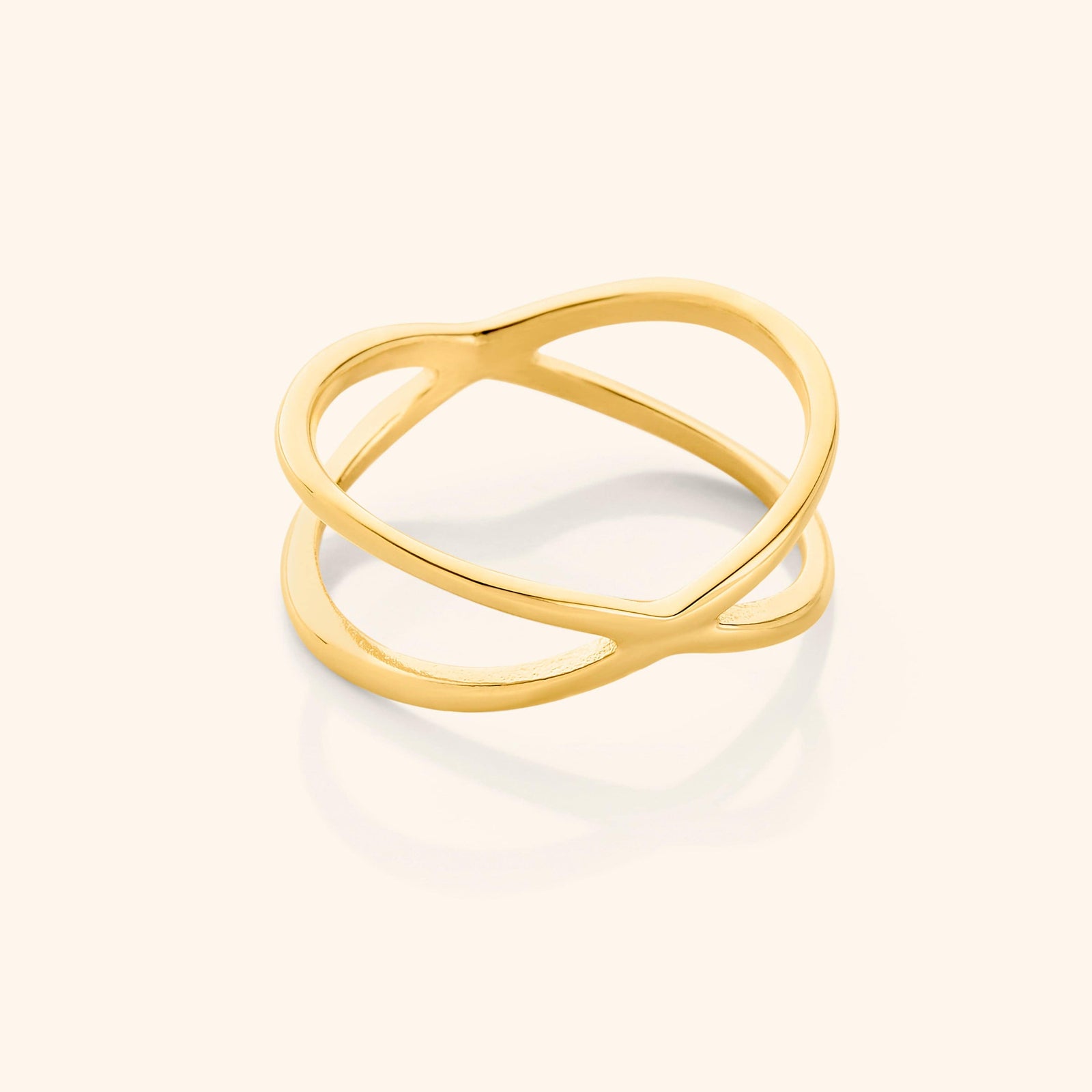 Close-up of a gold essential intersection ring on a neutral background, showcasing its criss-cross double-band design.