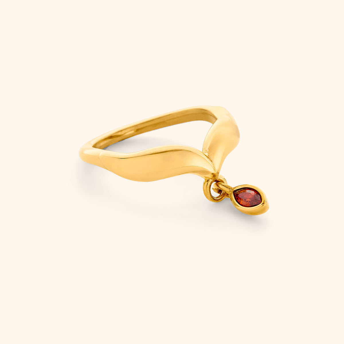 The Garnet Stone Keffiyeh Droplet Ring by Nominal, featuring a contoured 18k gold-plated band accented with a dangling bezel-set red garnet gemstone droplet, displayed on an off-white background.