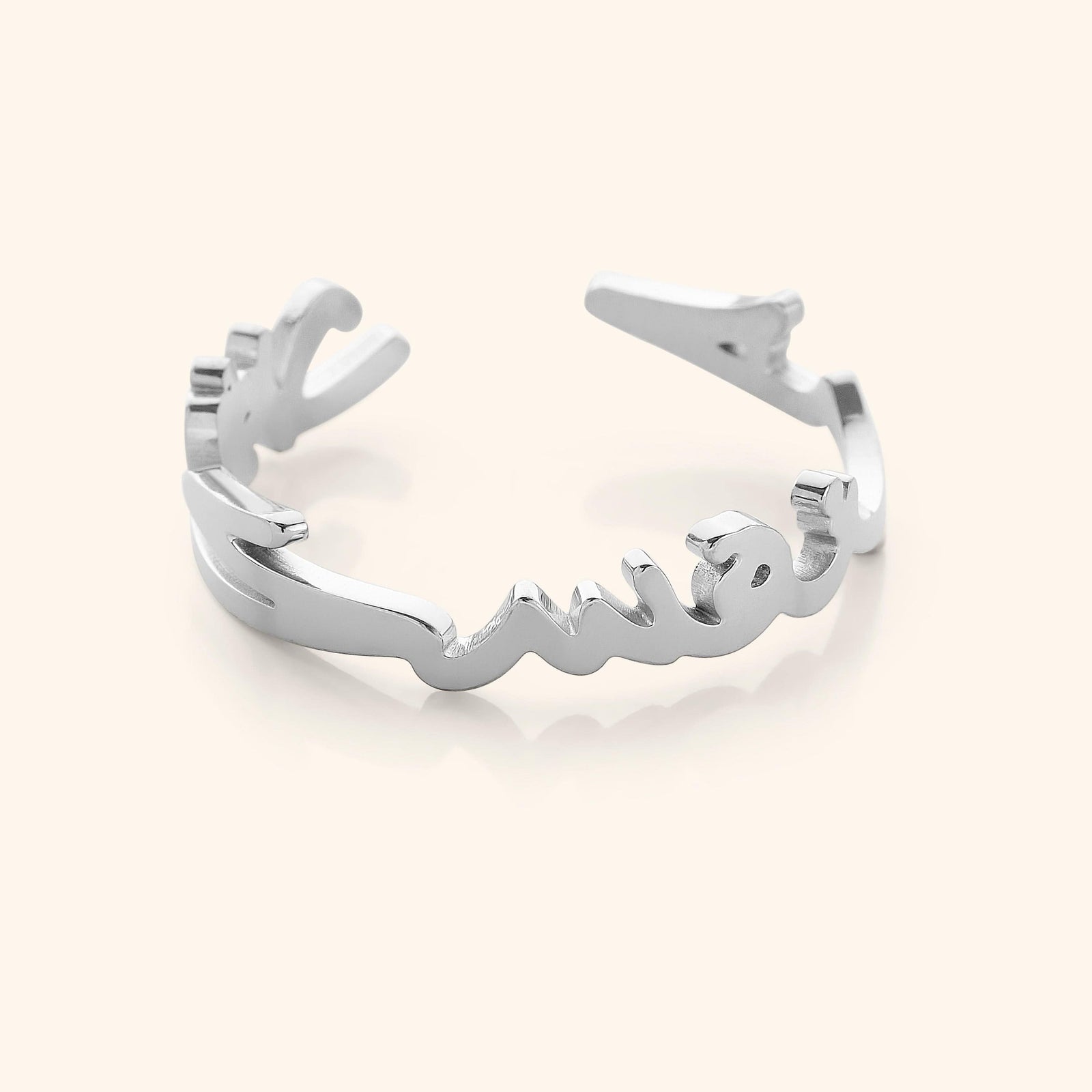 Close-up of a silver ring shaped into Arabic calligraphy spelling "Love Yourself First," on a neutral background.
