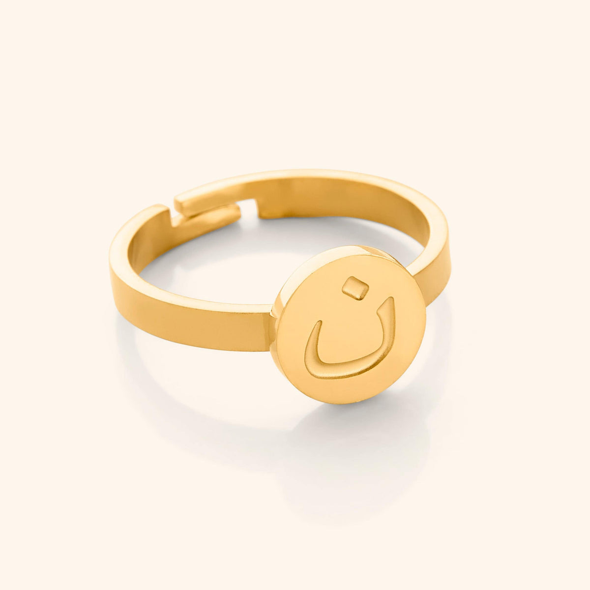 Close-up of a gold adjustable ring featuring a round face engraved with the Arabic letter (noon)