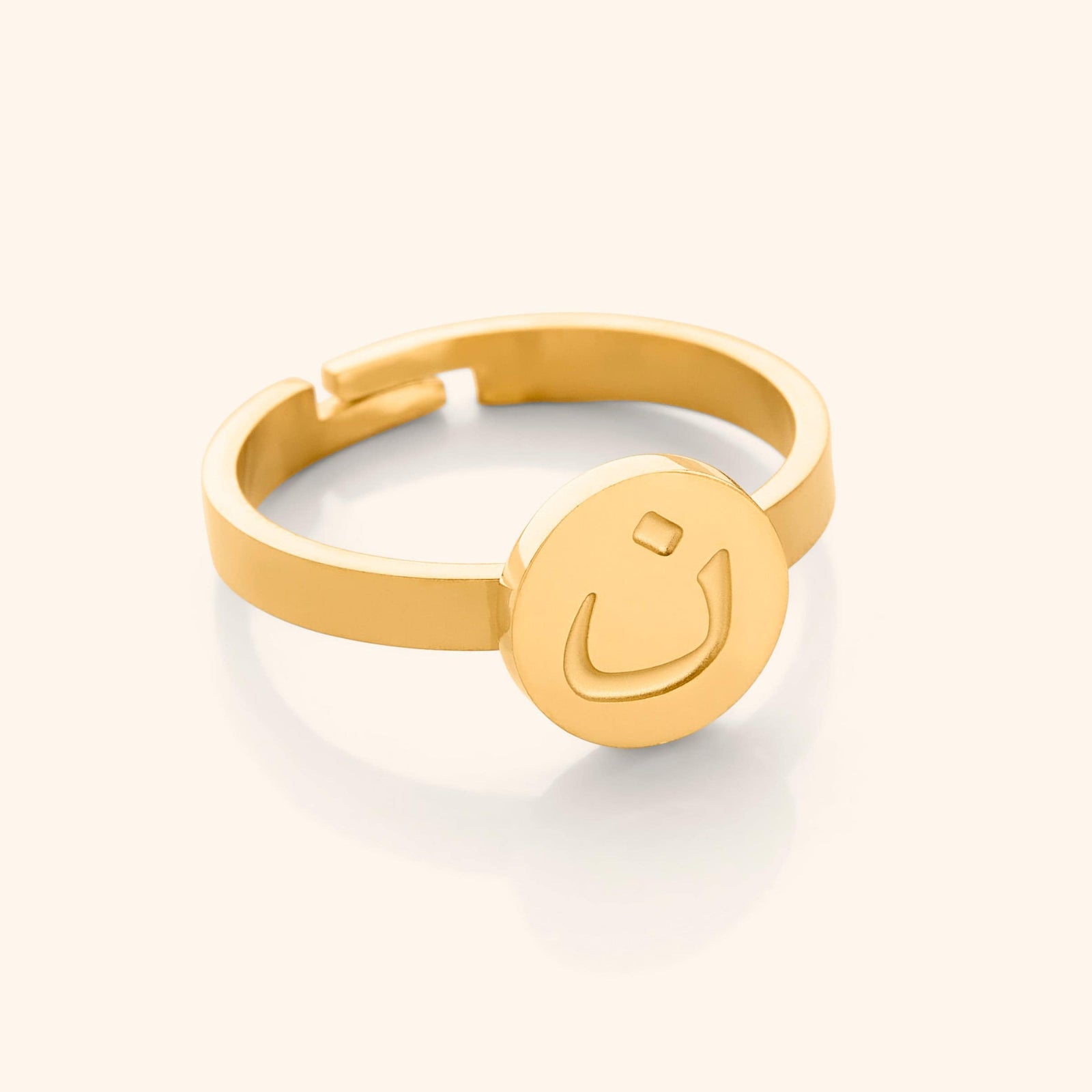 Close-up of a gold adjustable ring featuring a round face engraved with the Arabic letter (noon)