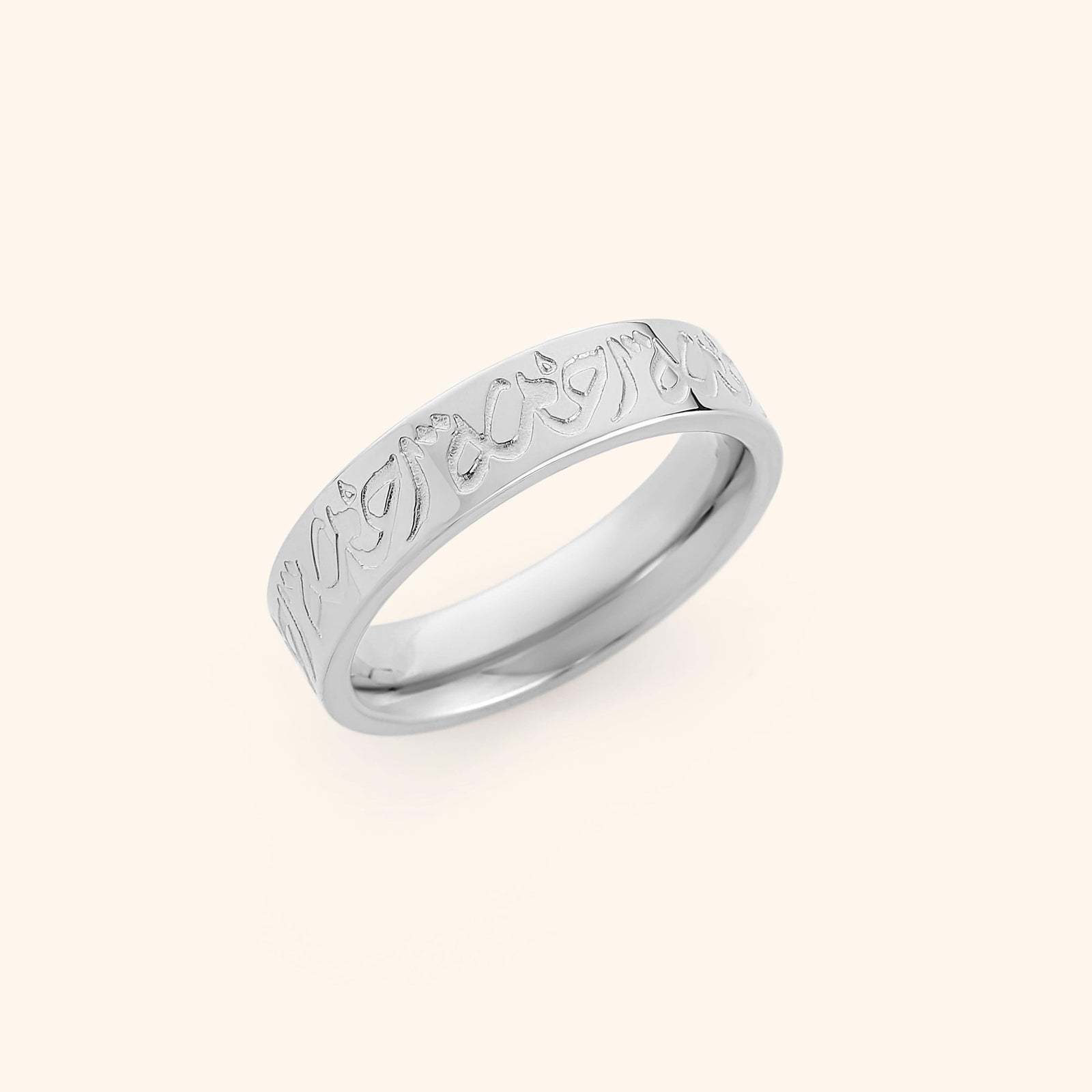 Silver band ring engraved with "Rahma" in Arabic calligraphy, displayed on a soft cream backdrop.