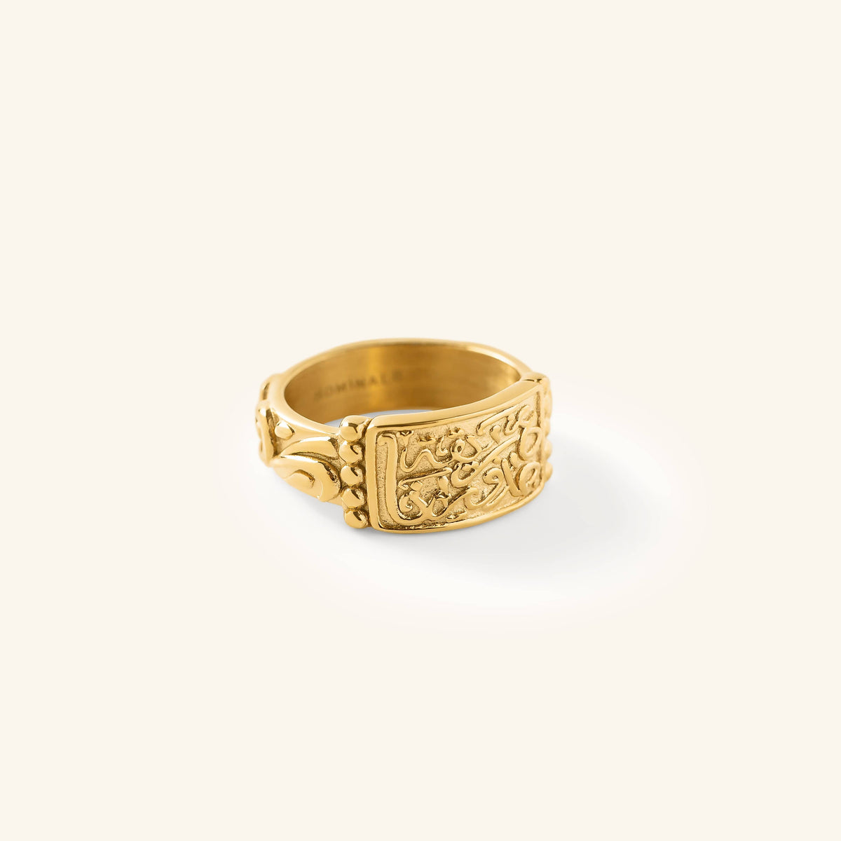Gold “Our Roots Run Deep” Ring featuring raised Arabic calligraphy and textured detailing across a wide band, shown against a neutral background.