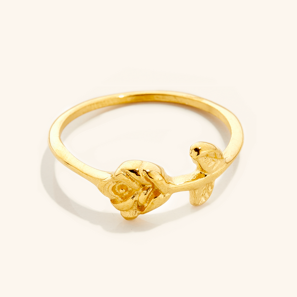 Gold ring featuring a delicate rose design with carved petals and leaves on a slim band, photographed against a neutral background.