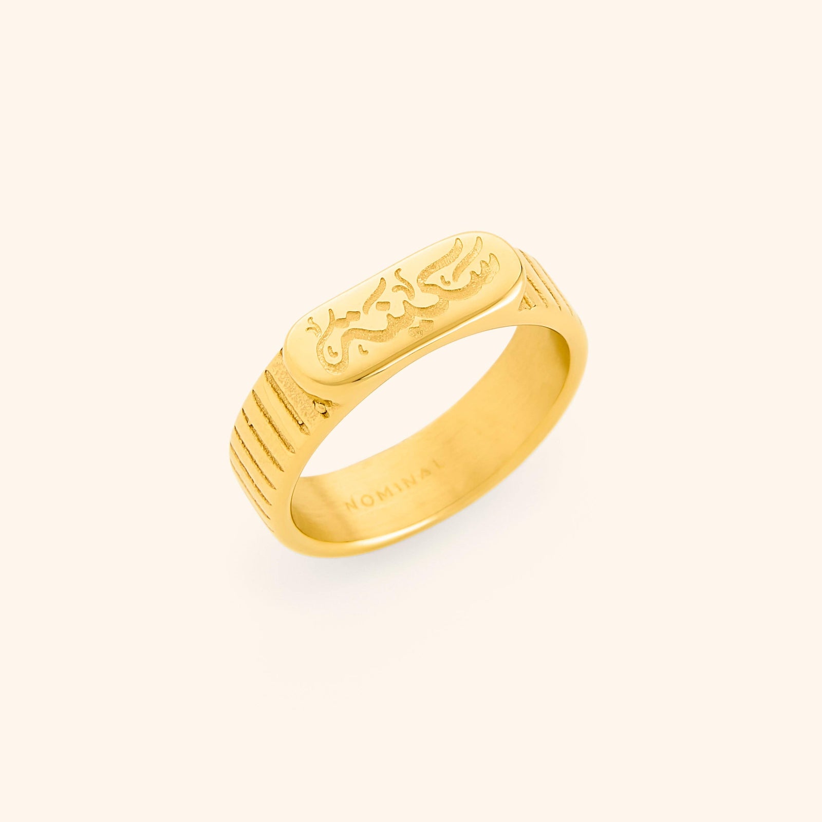 Gold ring with engraved “Sakinah” in Arabic calligraphy and lined side detailing. Inner of the band stamped with “NOMINAL.”