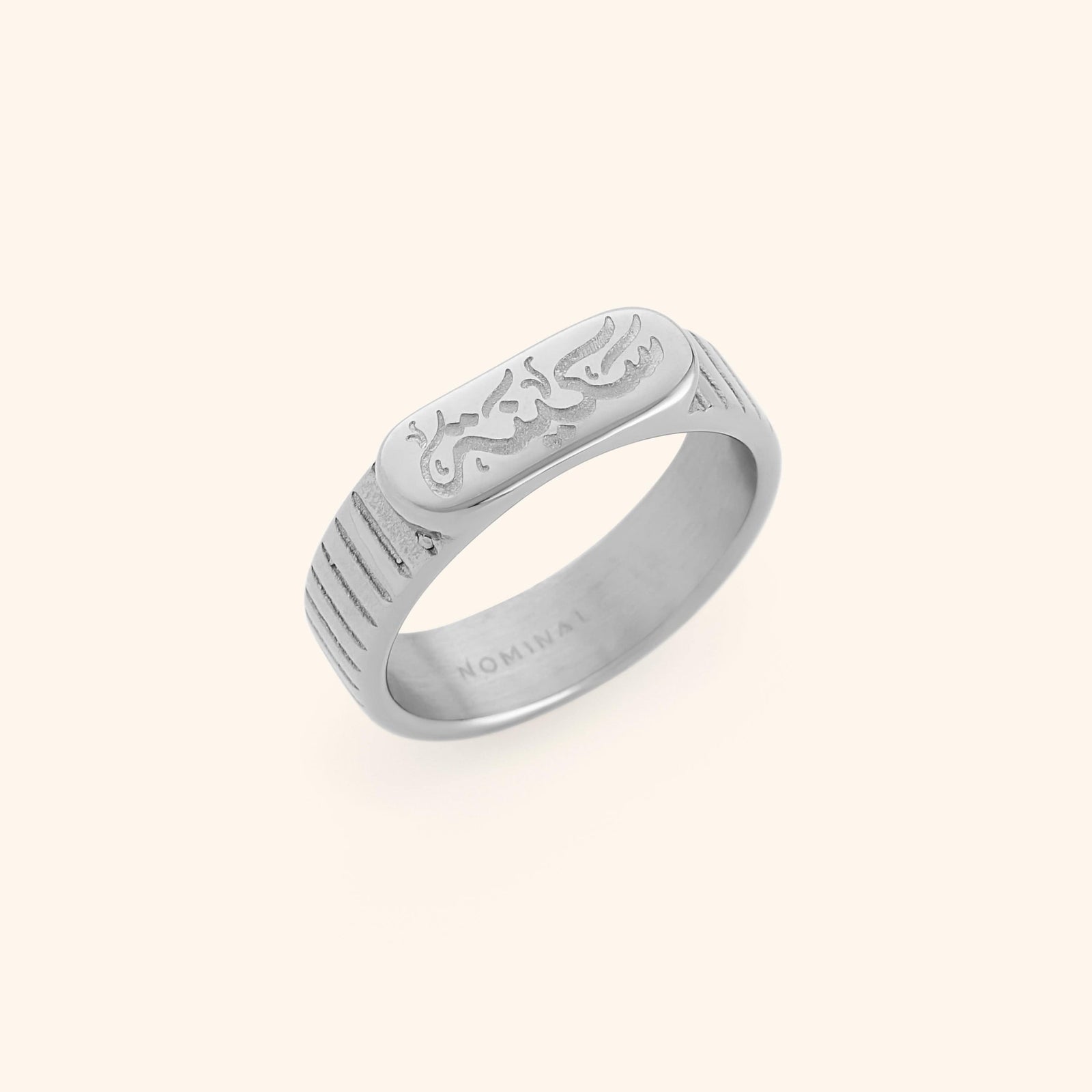 Silver ring with engraved “Sakinah” in Arabic calligraphy and lined side detailing. Inner of the band stamped with “NOMINAL.”